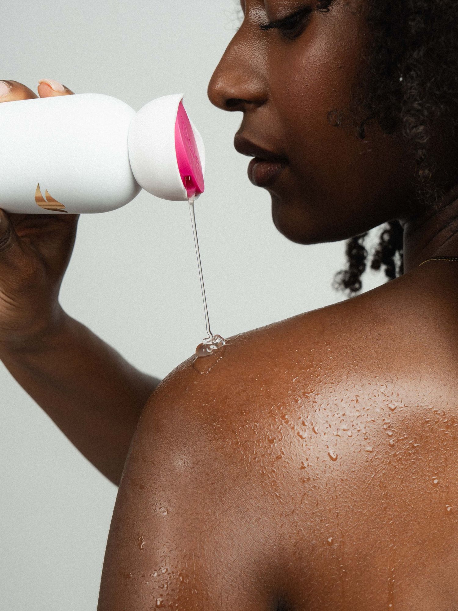 Woman applying liquid product from white bottle onto wet skin, showcasing a beauty or skincare routine.