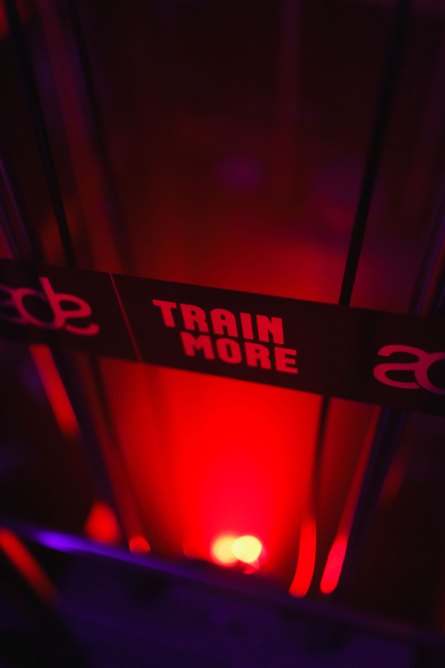 A glowing red Train More sign illuminated by vibrant red stage lighting in a dark venue.