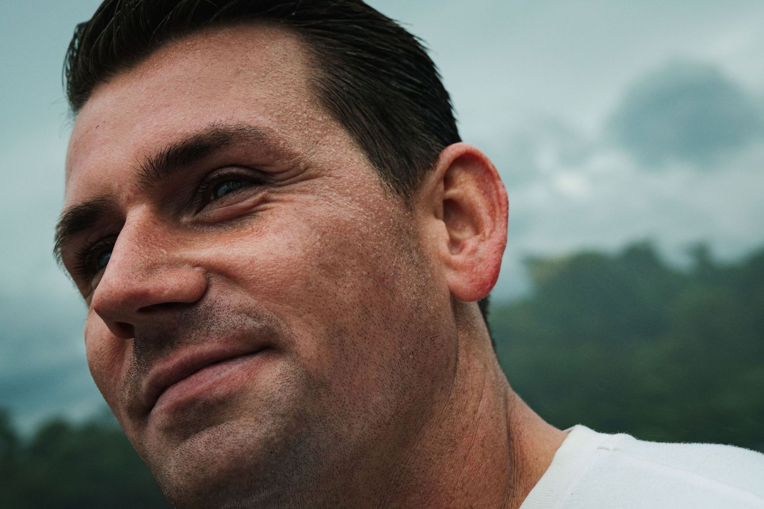 Close-up portrait of a smiling middle-aged man with dark hair wearing a white shirt outdoors.