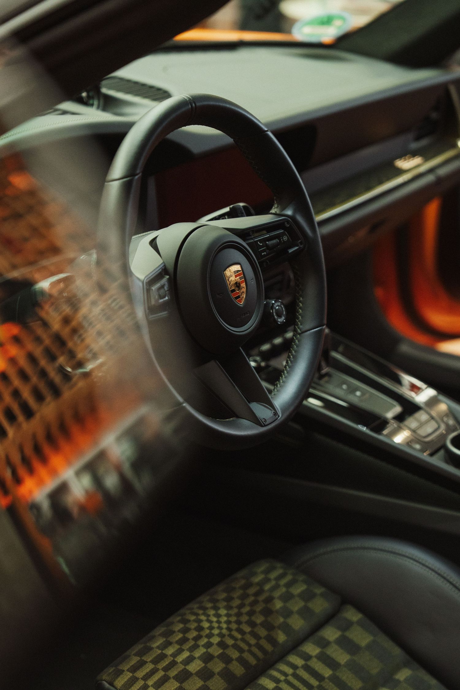 Porsche 911 interior featuring black leather steering wheel, sport seats, and orange carbon fiber trim accents.