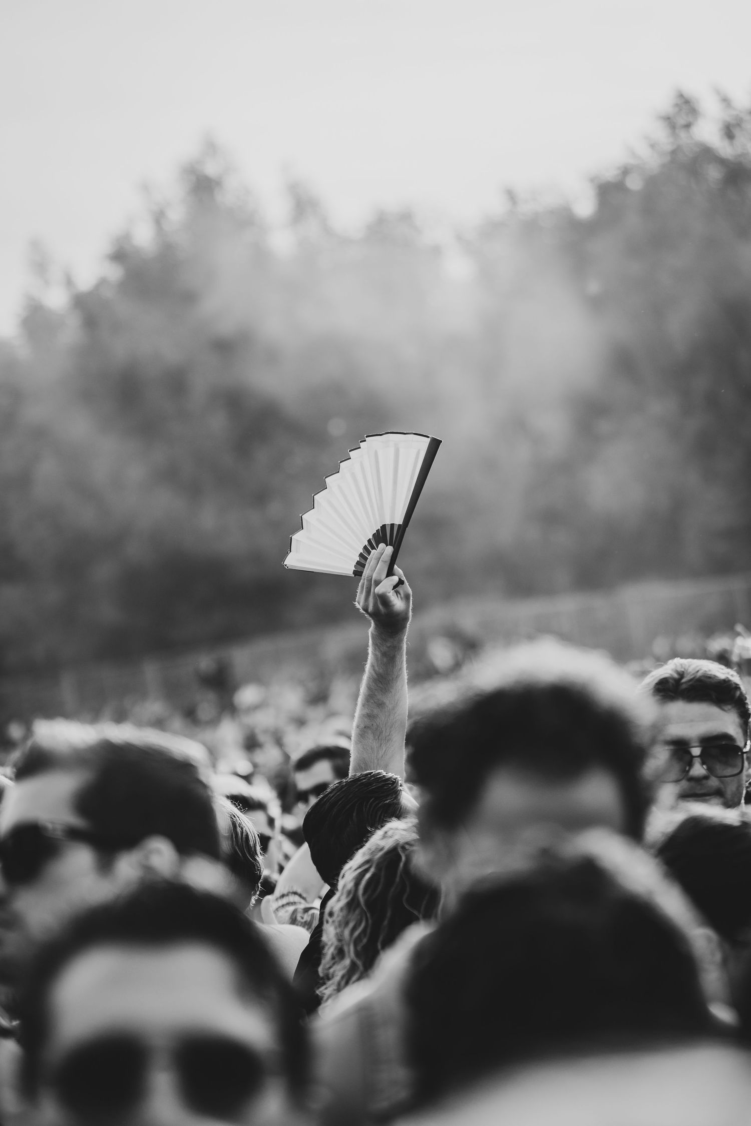 Black and white photo of a crowd at an outdoor festival, with one person raising a hand fan above the crowd.