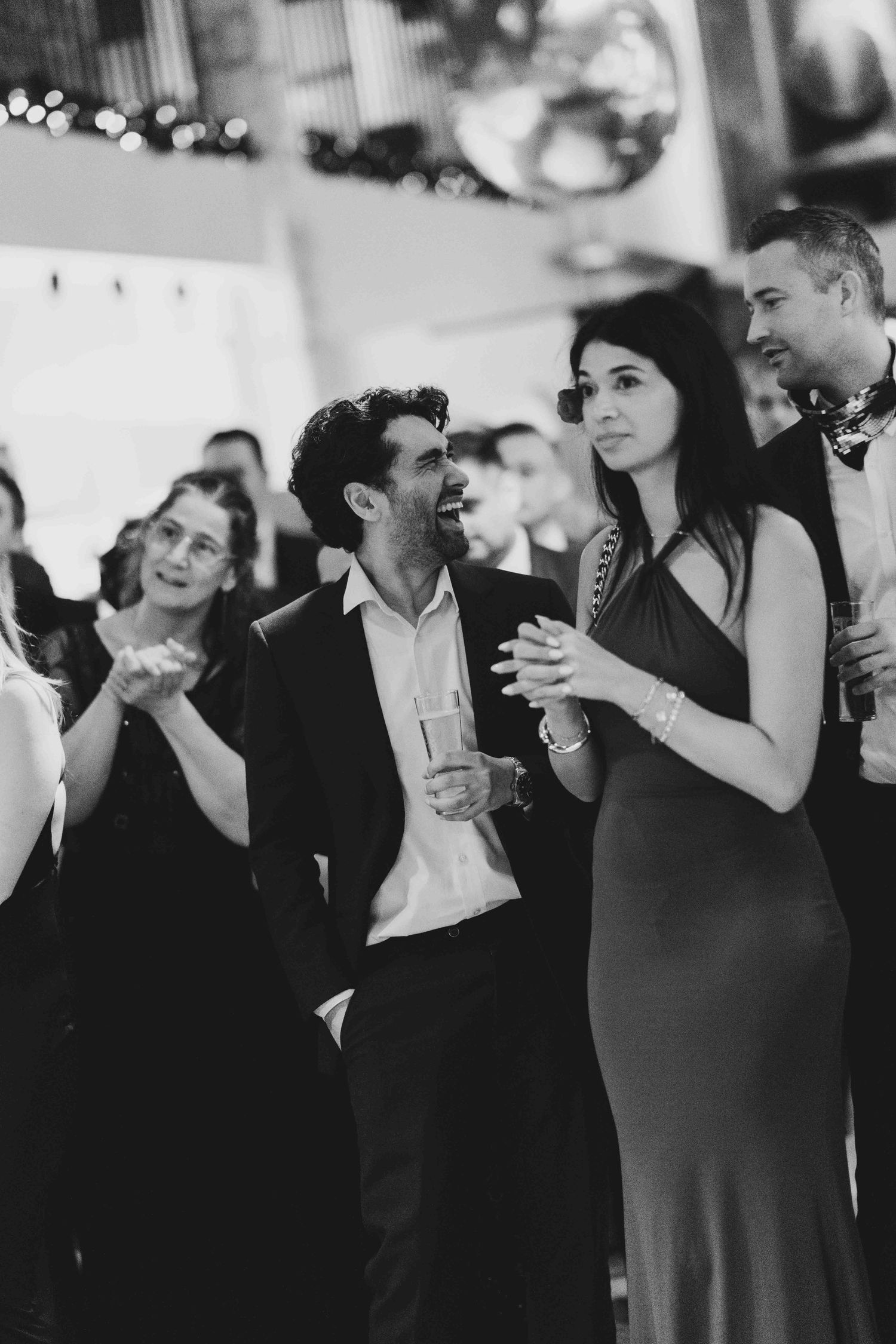 Black and white photo of elegantly dressed guests laughing and clapping at a formal evening event.