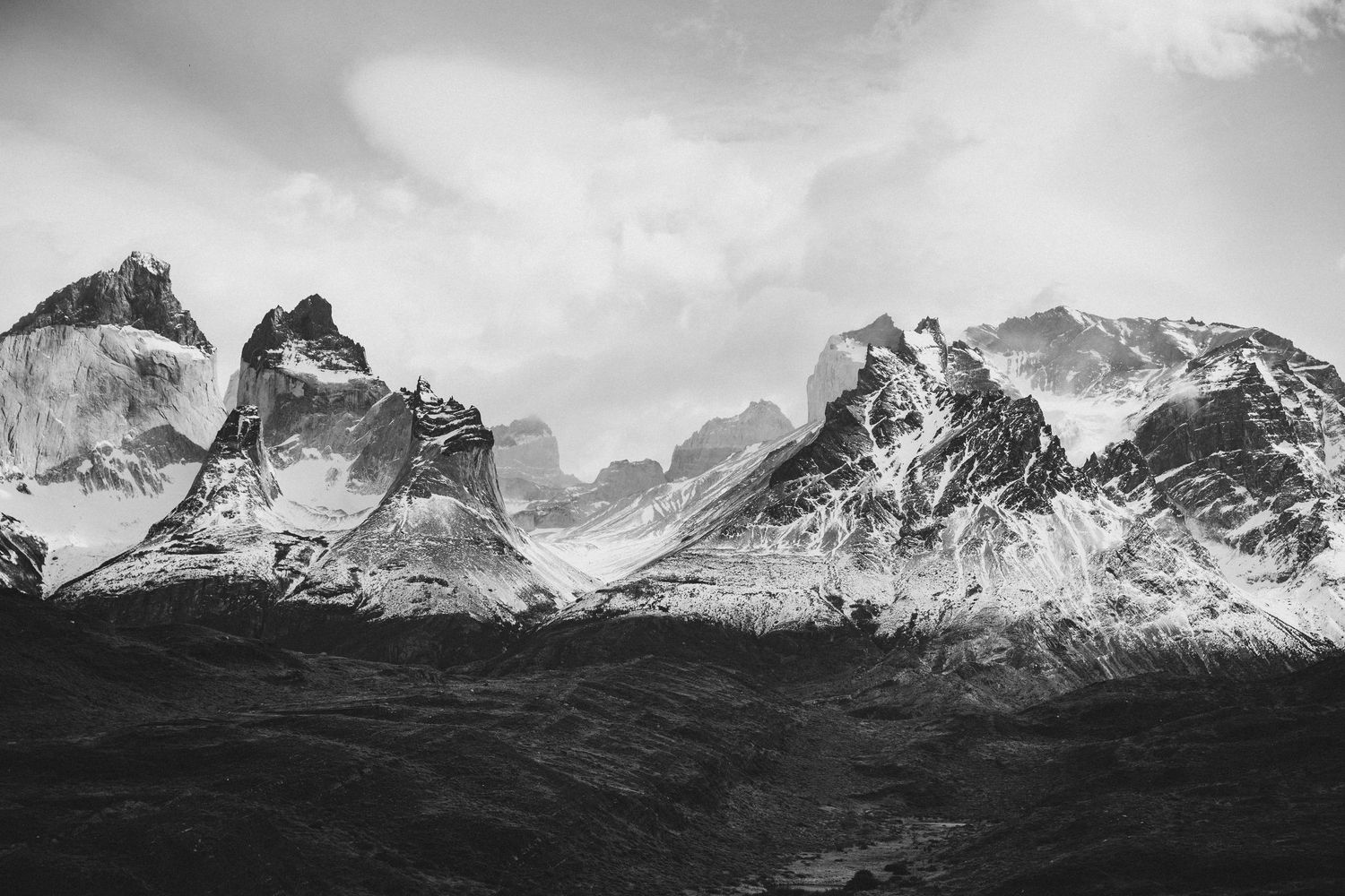Black and white photo of snow-capped mountain peaks in Torres del Paine, Patagonia, under a cloudy sky.