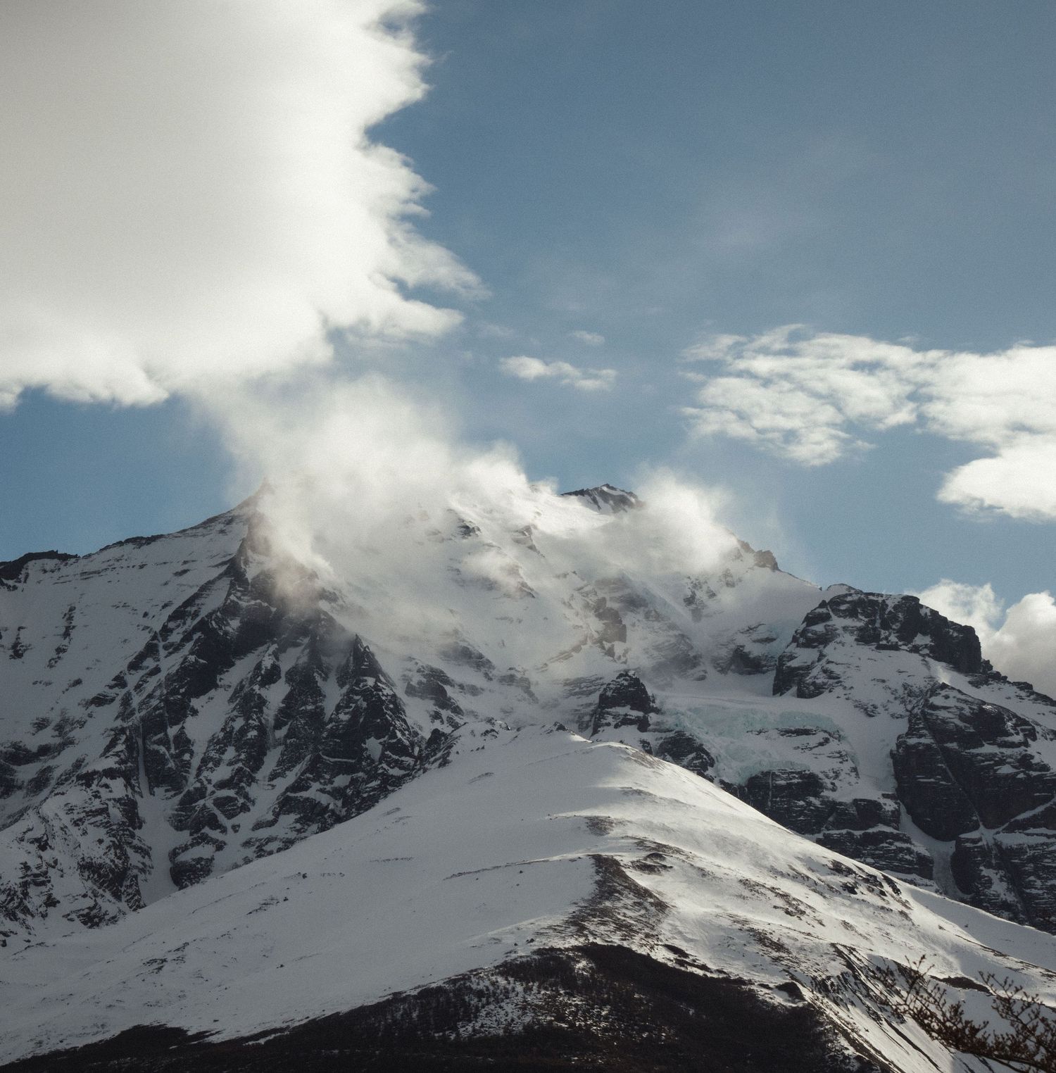 Snow-capped mountain peaks partially shrouded in dramatic clouds against a blue sky in a stunning alpine landscape.