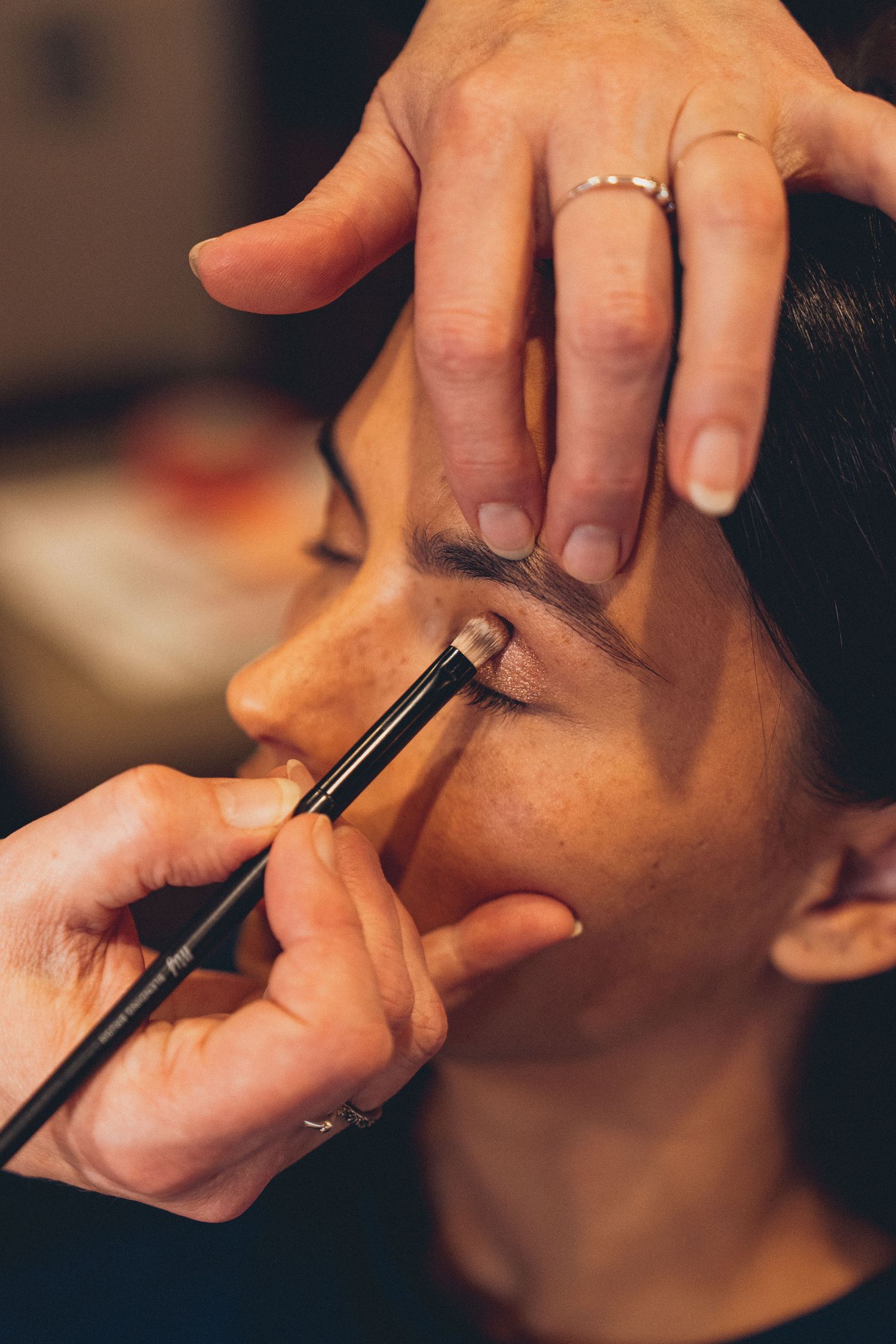 Makeup artist applying eyeshadow with a brush to a woman's eyelid during a professional makeup session.