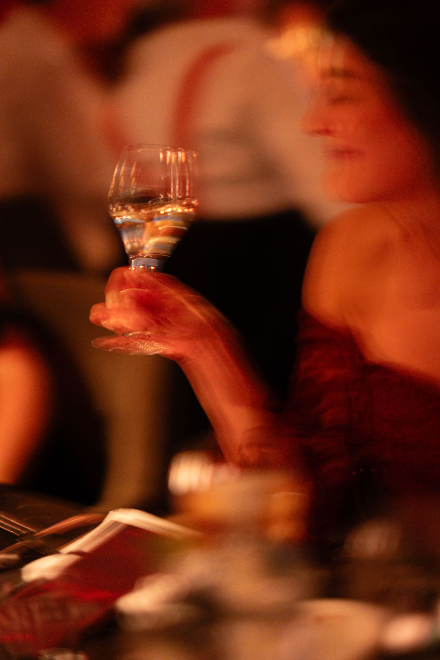A blurred woman in a red dress holds a wine glass at an elegant evening event.
