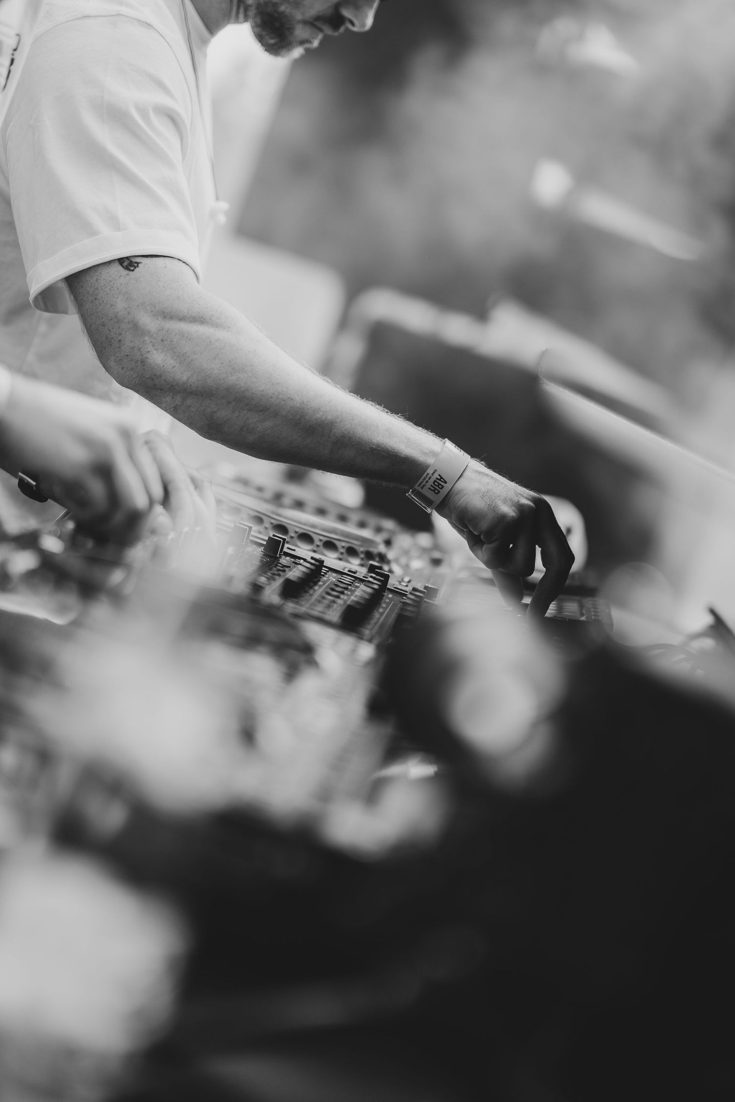 Black and white photo of a DJ mixing music on turntables at an outdoor event.