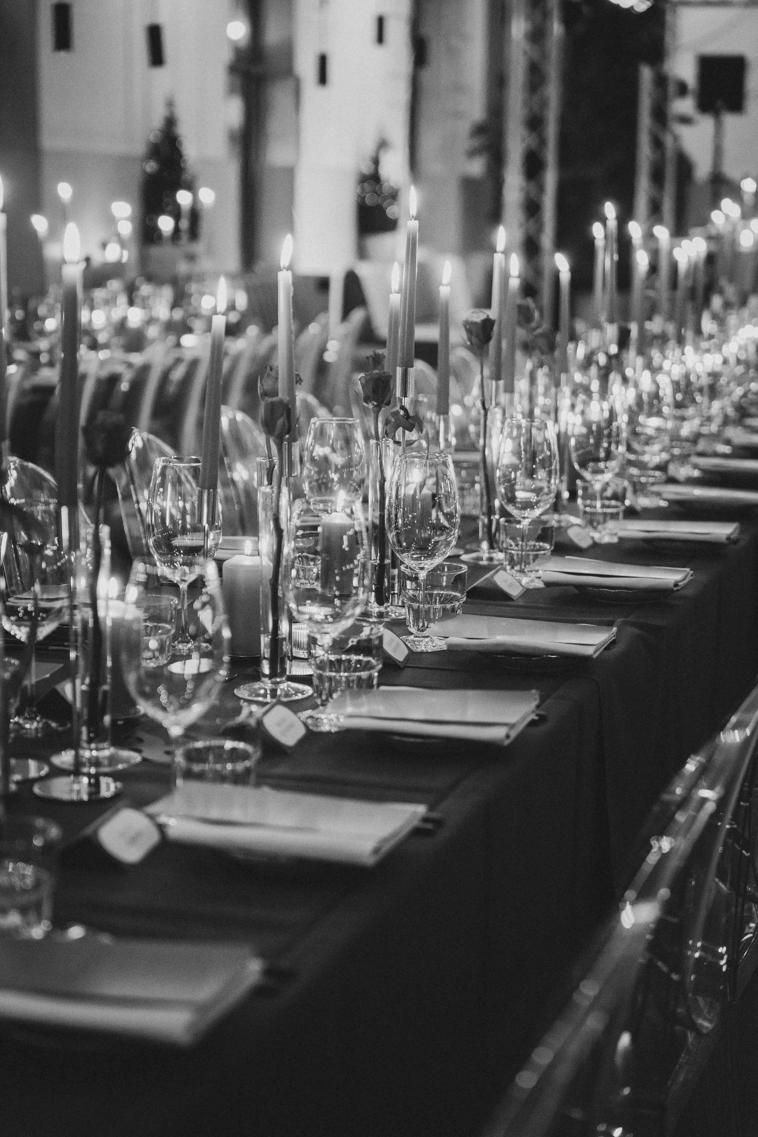 Black and white photo of an elegant long dining table set with candles, crystal glasses, and formal place settings.