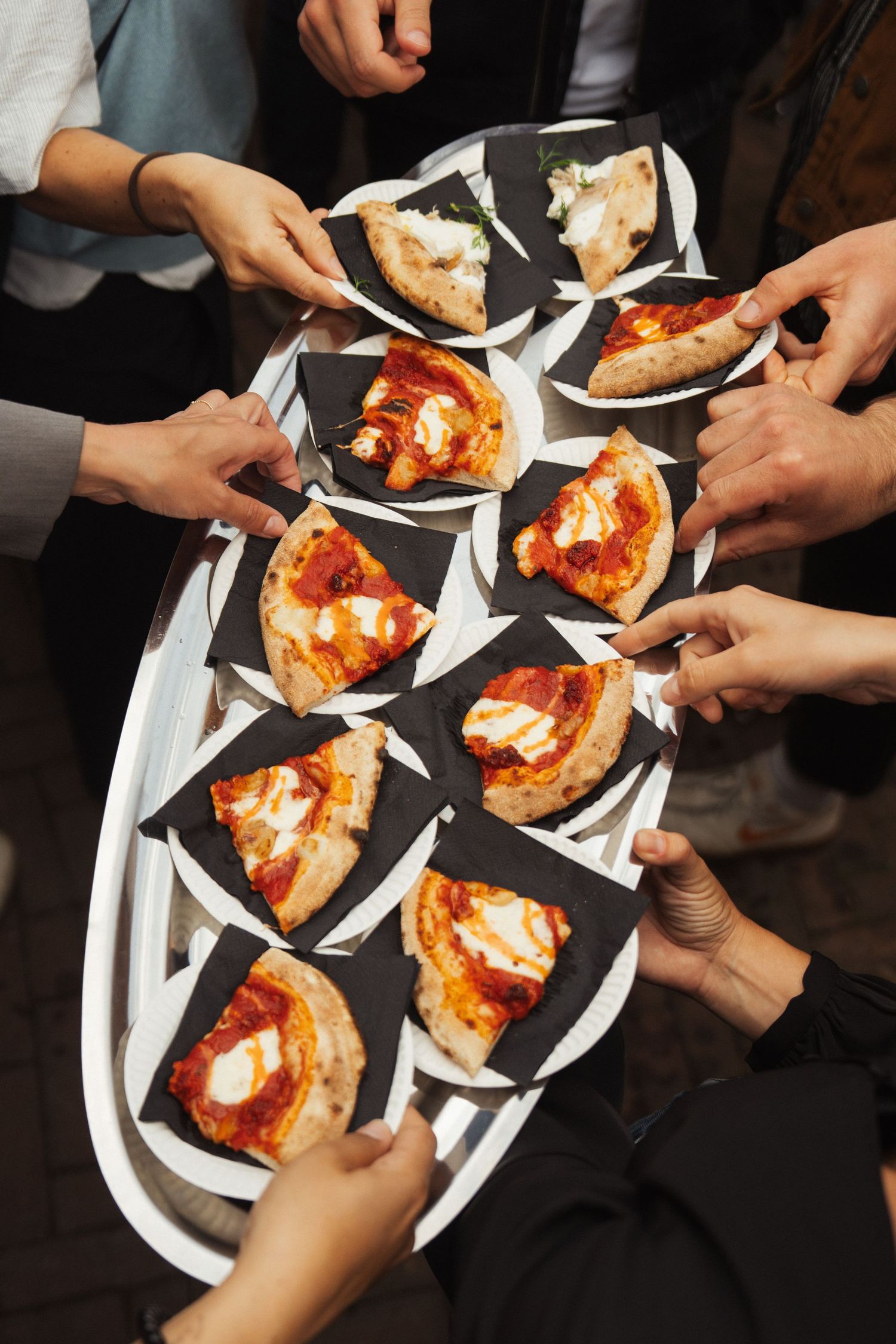 Hands reaching for pizza slices on a serving tray at a catered event.