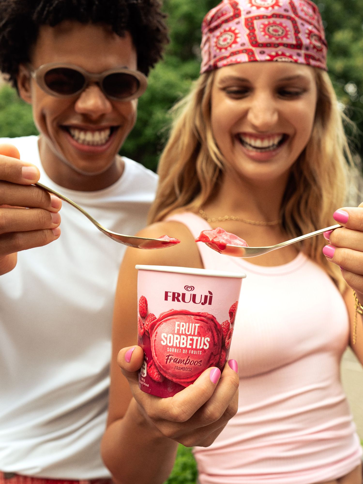 Two friends smiling and sharing a Fruuji raspberry fruit sorbetus ice cream cup outdoors.