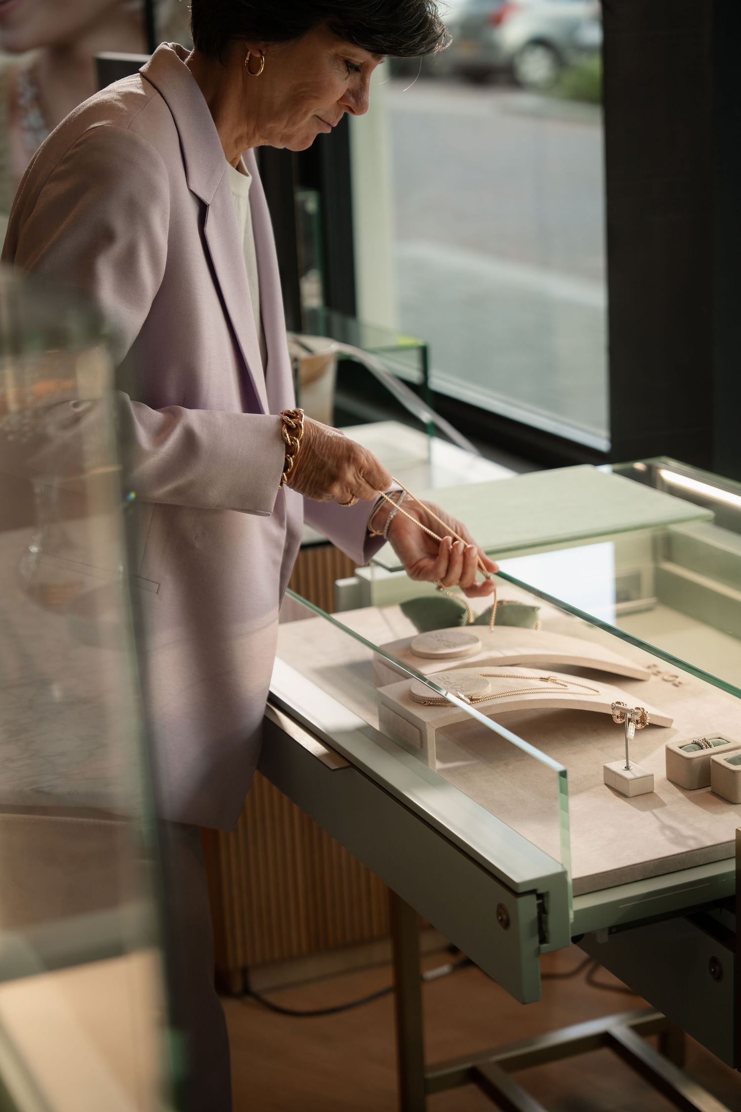 Elegant woman in lavender blazer examining jewelry display in upscale boutique store.