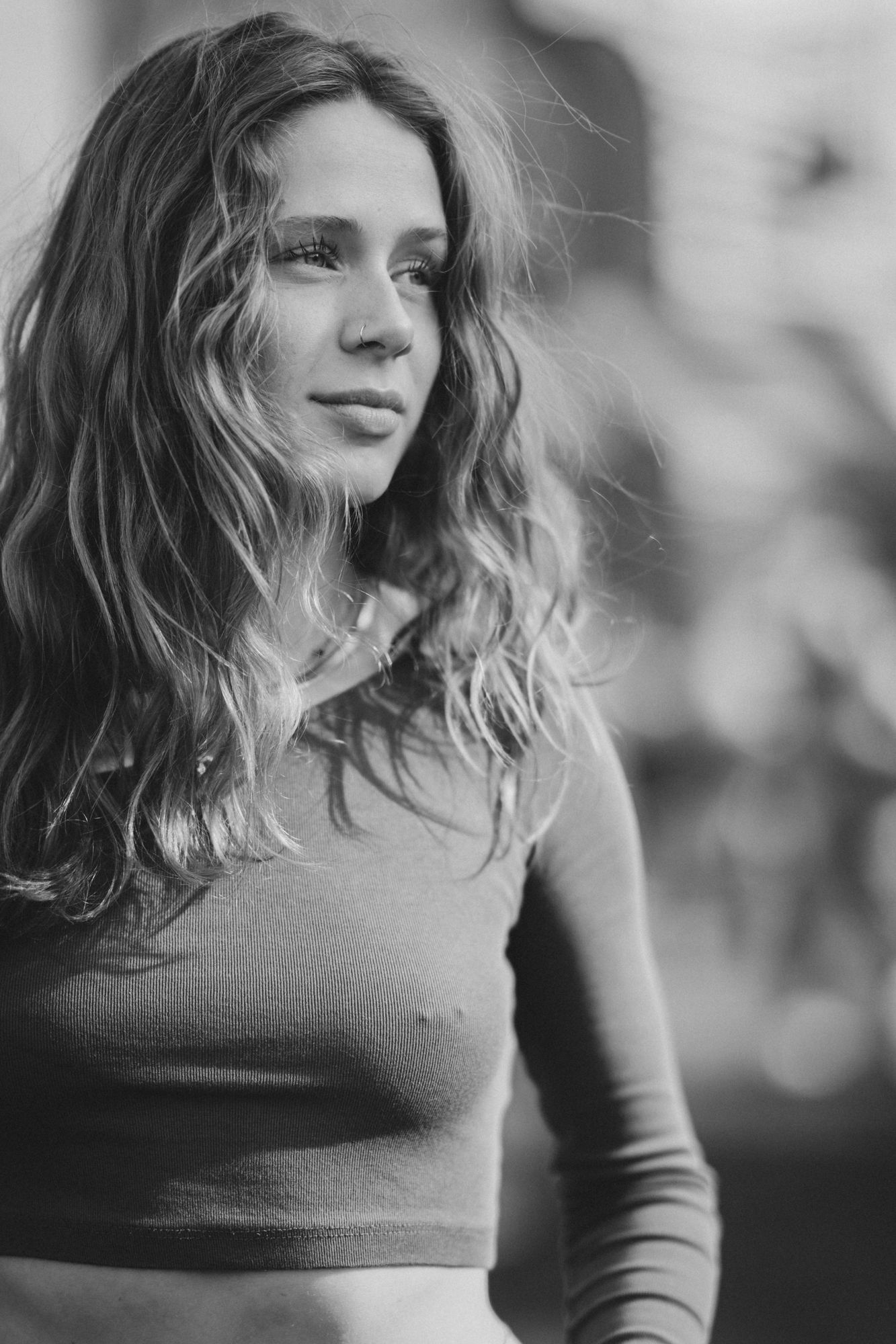 Black and white portrait of a young woman with wavy hair wearing a fitted top, looking away softly.