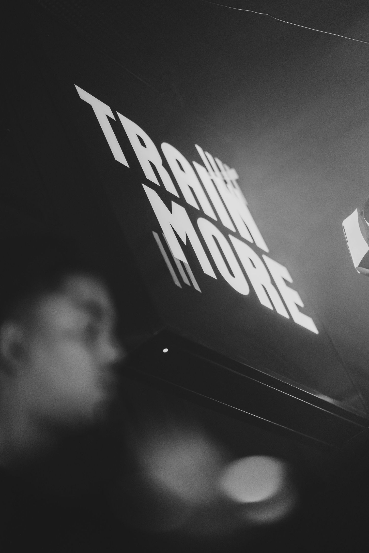 Black and white photo of illuminated Train More sign in dark gym.
