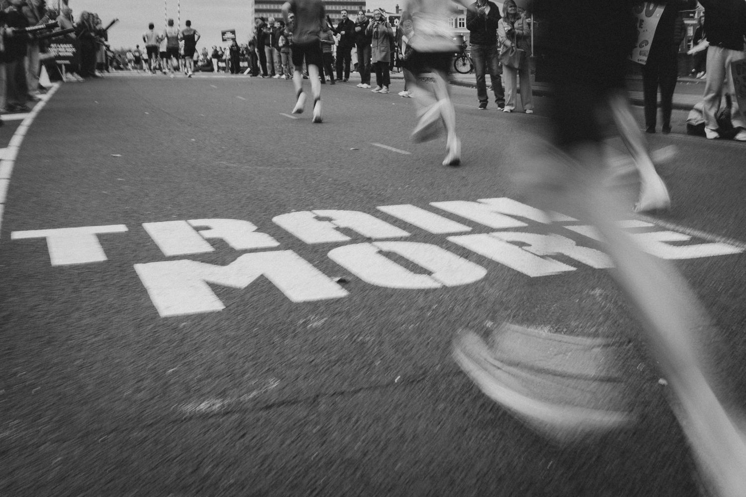 Black and white motion shot of runners passing over text painted on street.