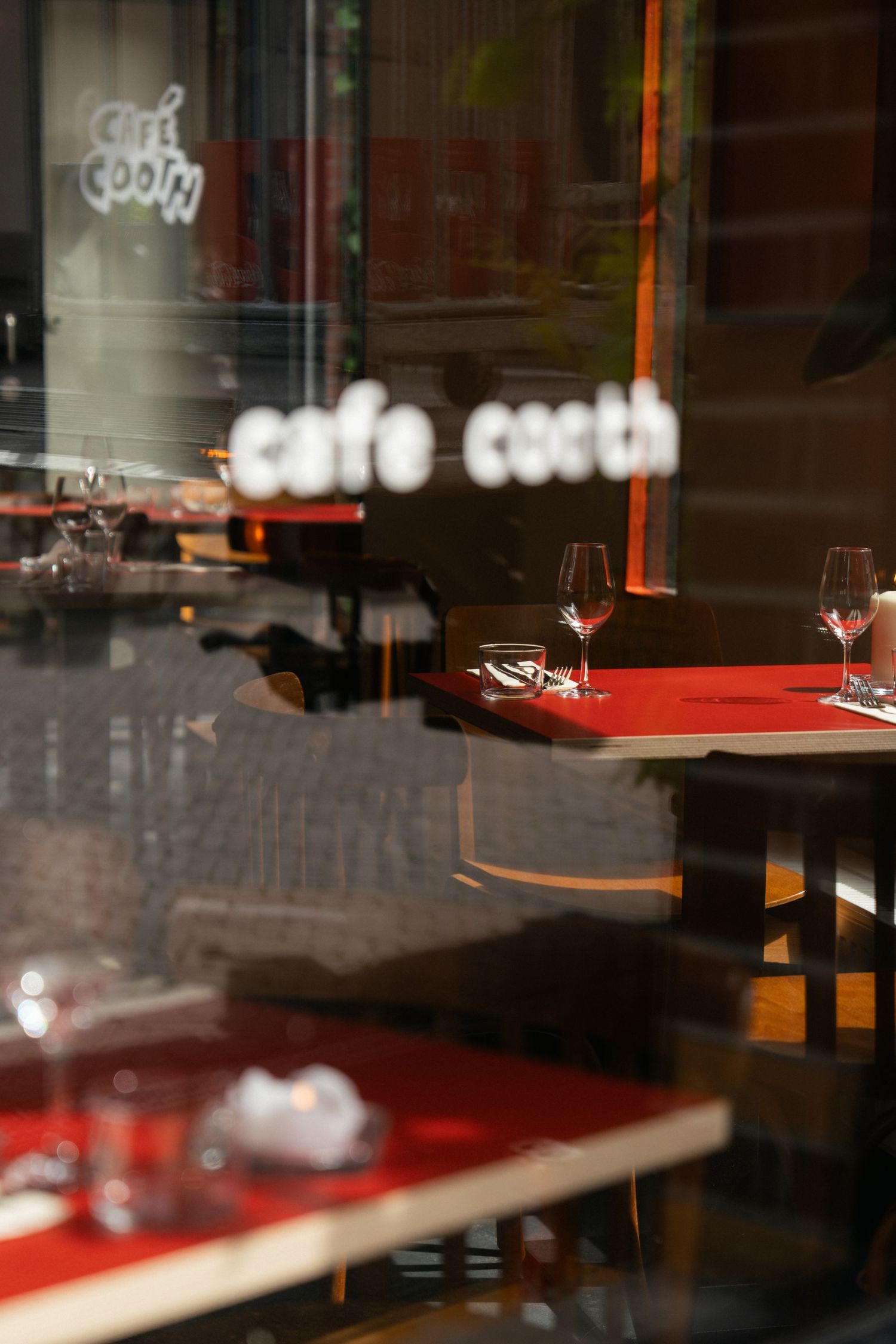 Interior view of Cafe Cocth through window, showing red-topped tables set with wine glasses in an elegant dining setting.