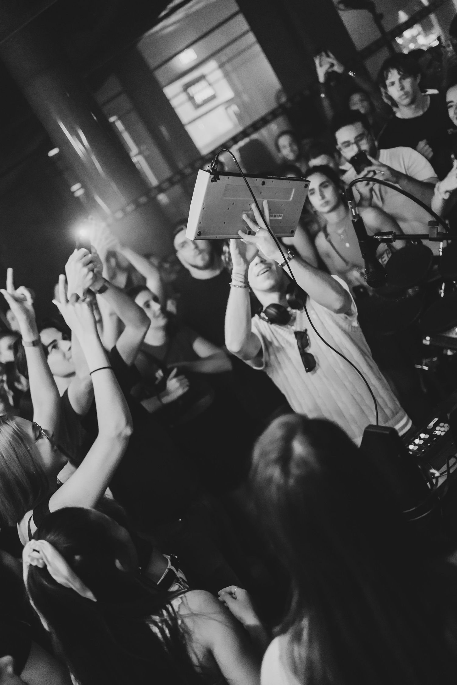 Black and white photo of a crowd at a concert, with someone holding a tablet above their heads to capture the event.