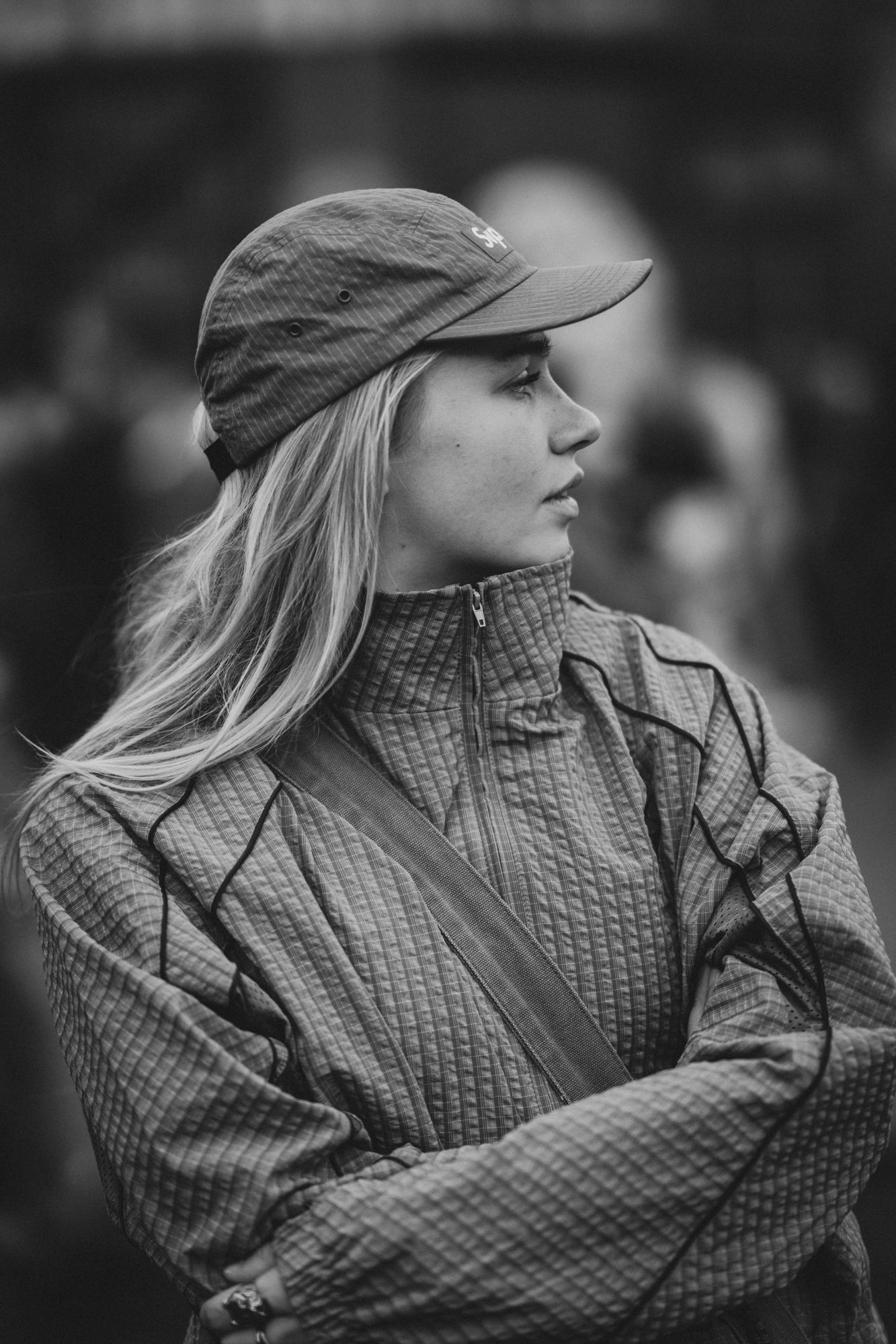 Black and white portrait of a young blonde woman wearing a cap and textured jacket with arms crossed.