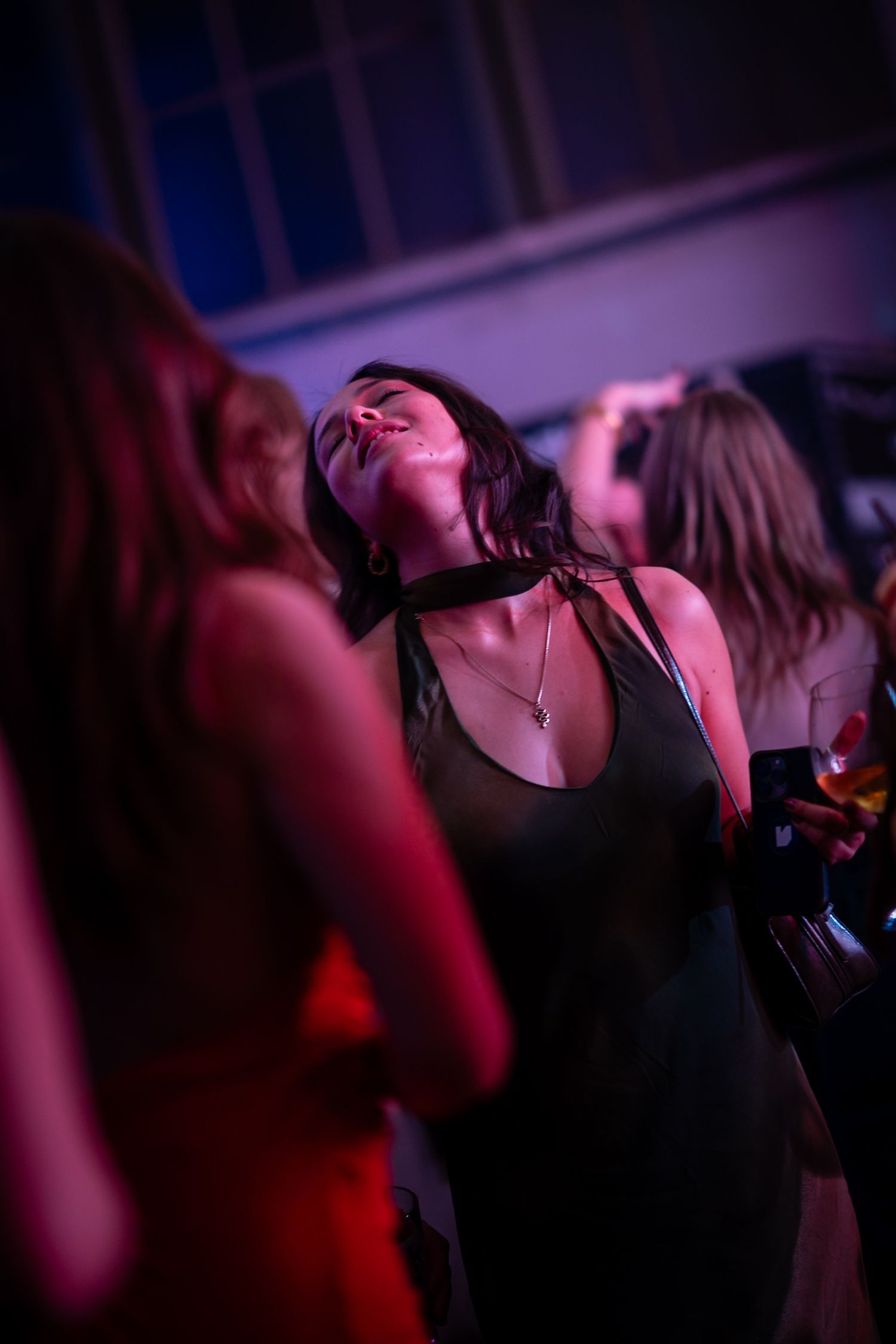 Woman dancing with eyes closed under purple lights at a vibrant nightclub event.