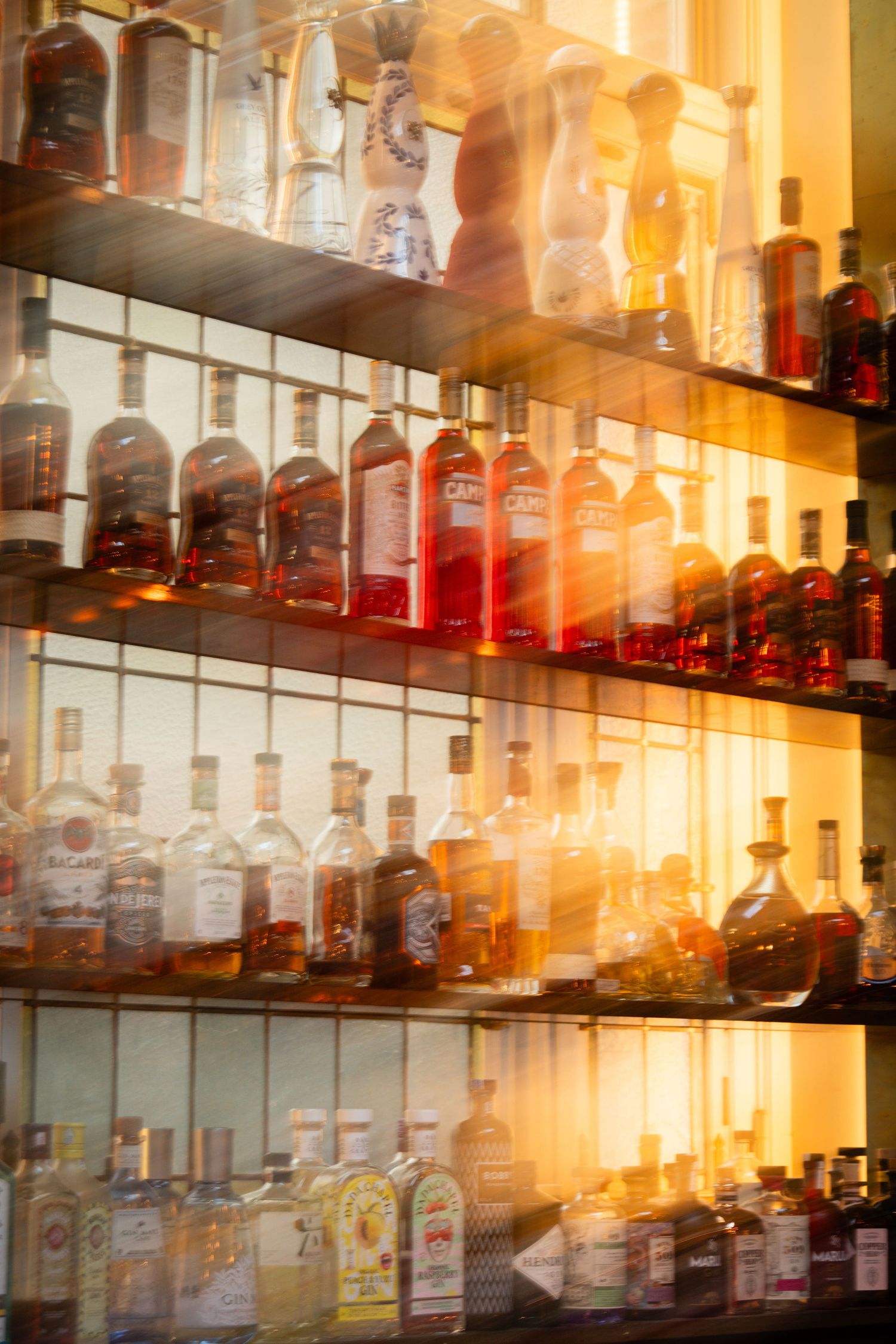 Warmly lit bar shelves displaying rows of assorted liquor bottles with a golden bokeh effect.