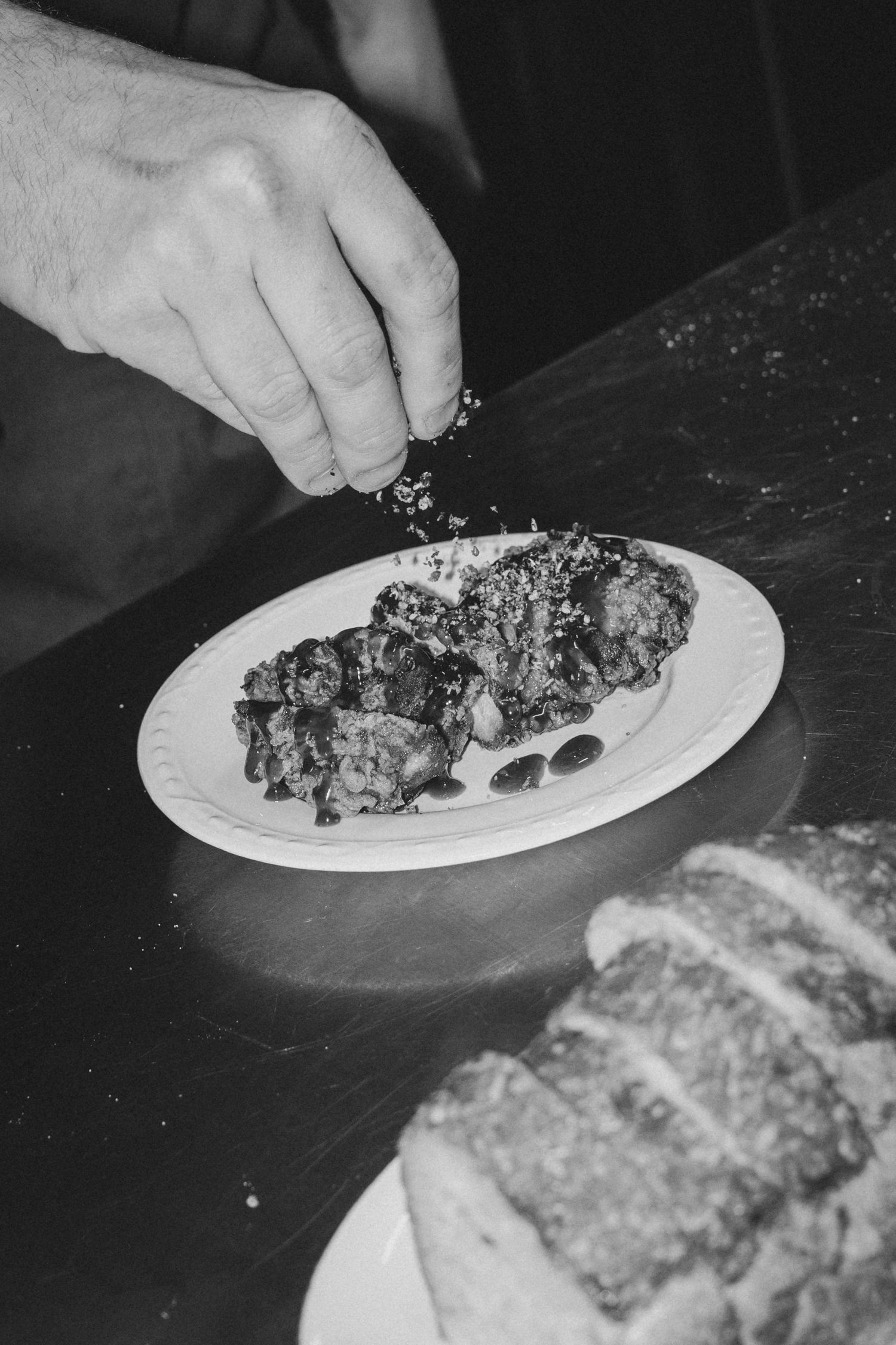 Chef hand seasoning gourmet meat dish with bread on dark wooden table, black and white.