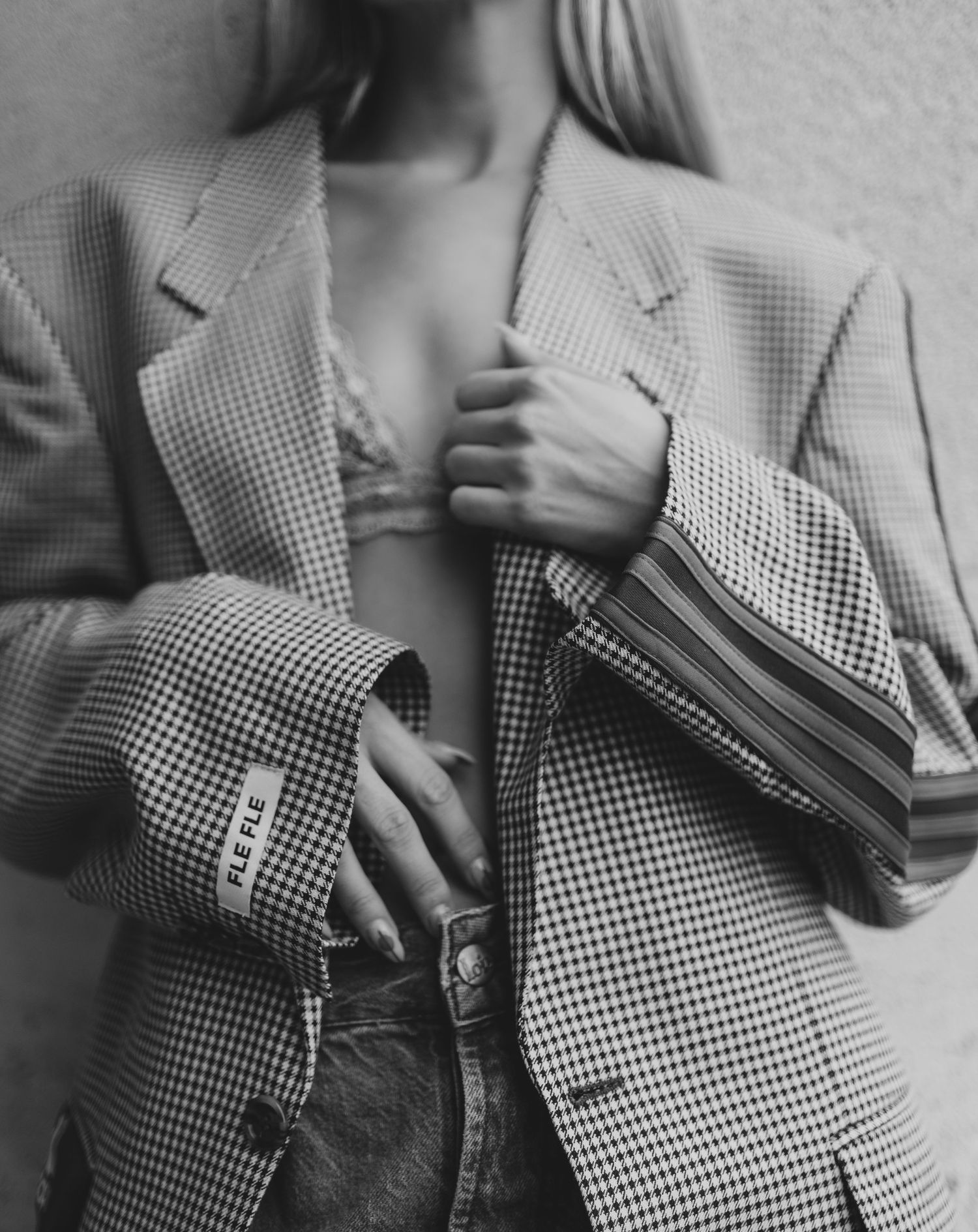 Black and white photo of woman in oversized houndstooth blazer with striped cuffs, hands crossed over chest.