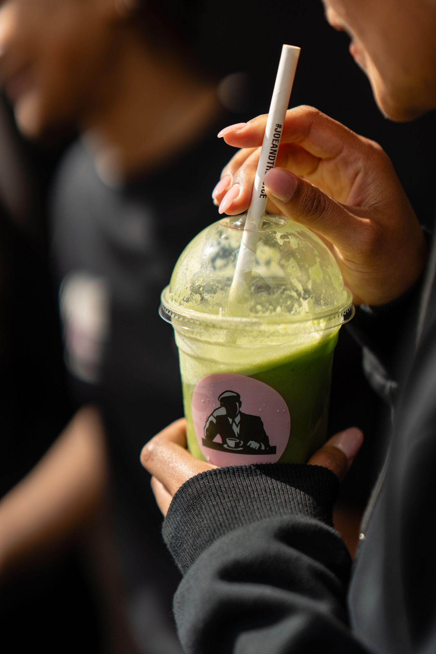 Person holding a green matcha smoothie drink with a straw in a branded plastic cup.