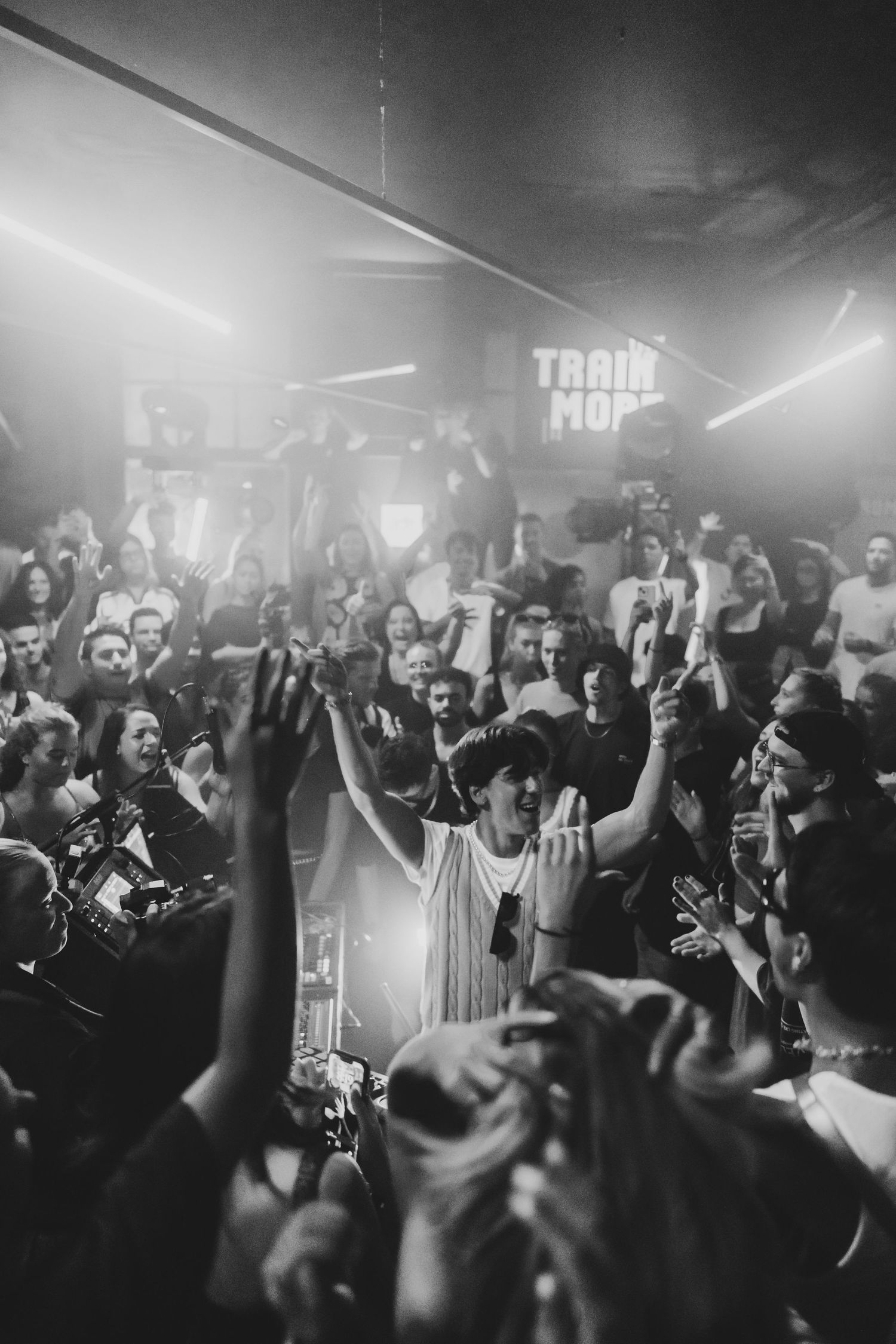Black and white photo of a performer with raised hands energizing a packed concert crowd.