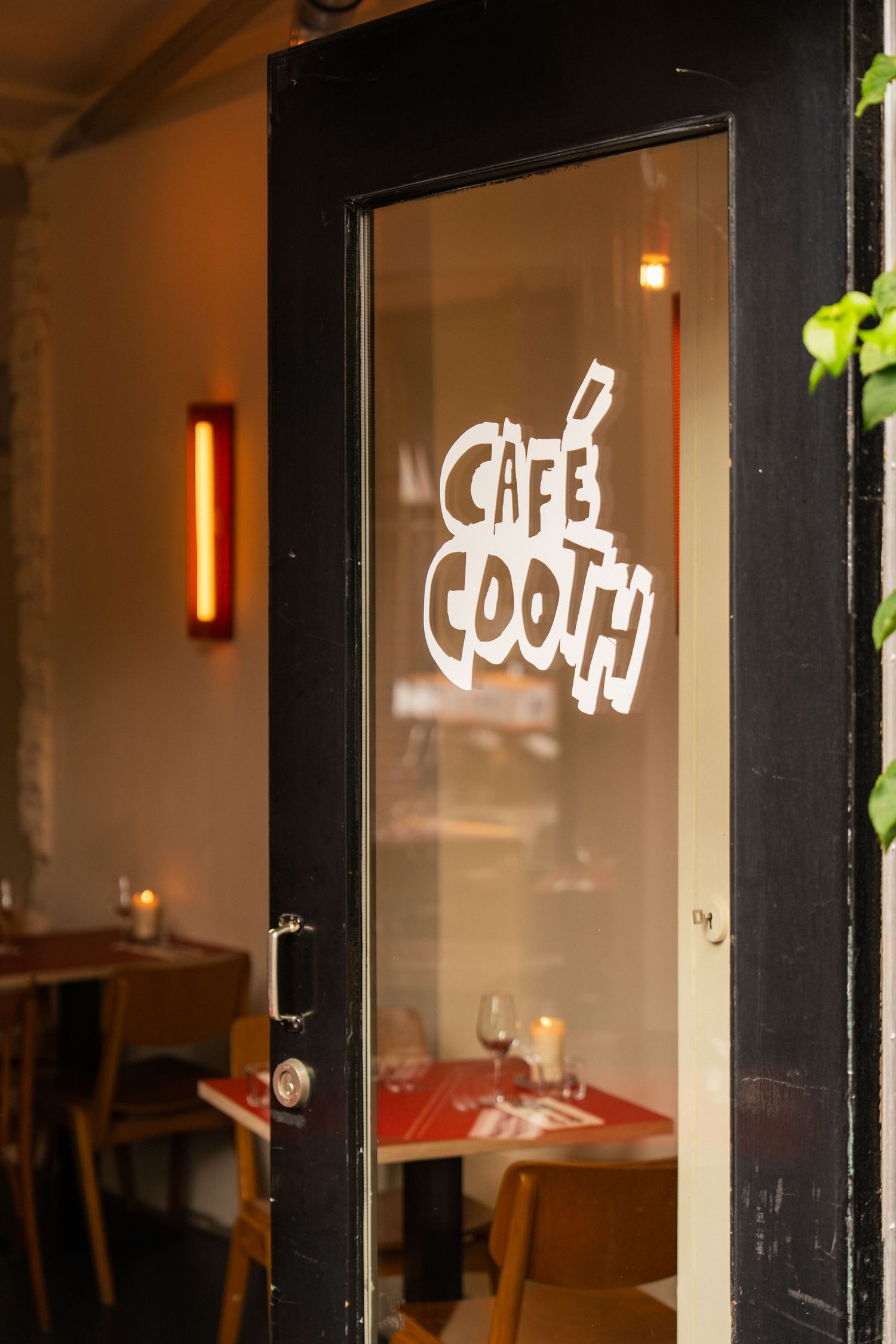 Glass door of Café Cooth restaurant with white logo lettering, revealing warmly lit dining tables inside.