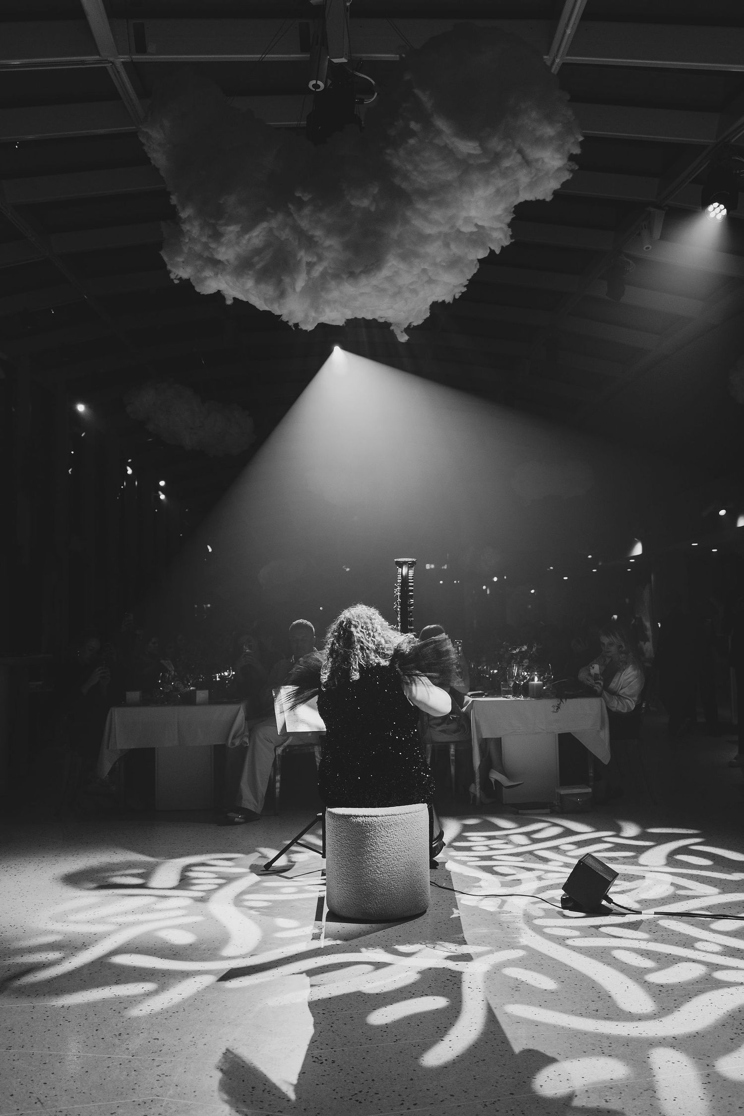Black and white photo of a person seated at a dimly lit event venue with dramatic spotlight and decorative floor projections.