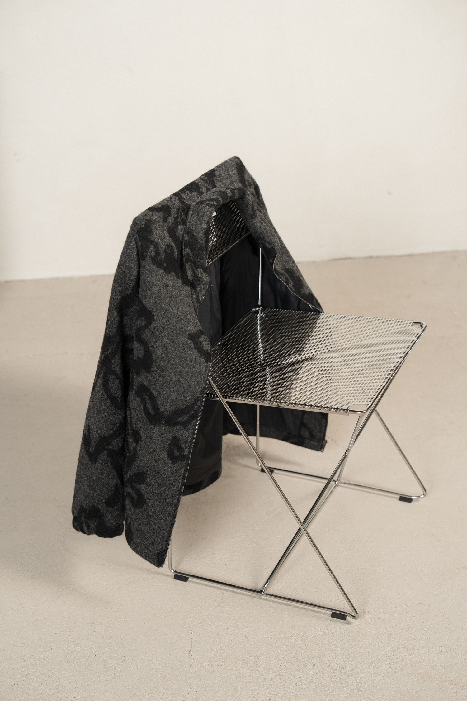 A series of black folding chairs with a black jacket draped over them shown in different angles against a white background.