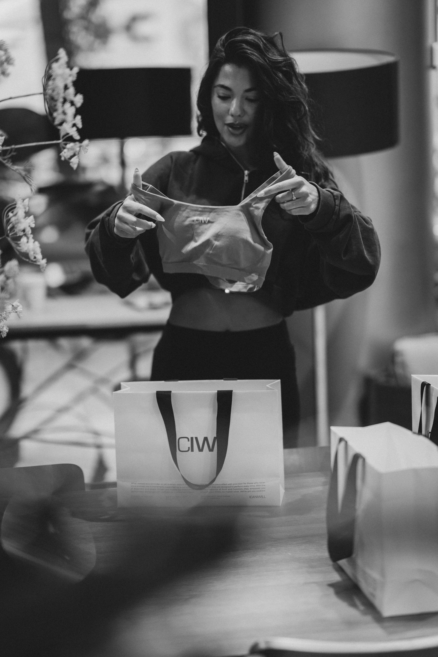 Woman in oversized jacket opening shopping bags on a table in black and white photo.