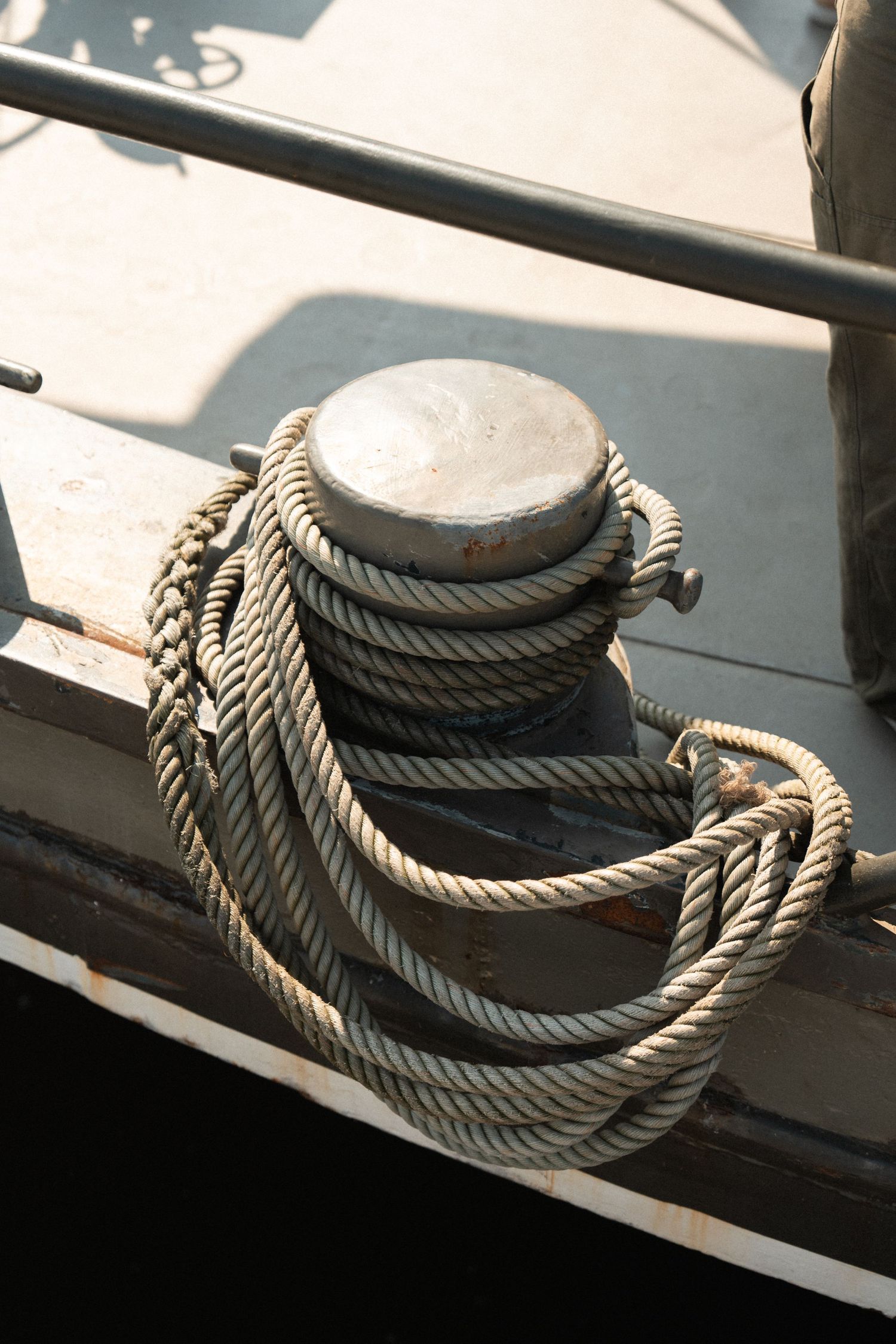 Thick rope coiled around a weathered metal bollard on a wooden boat deck near the railing.