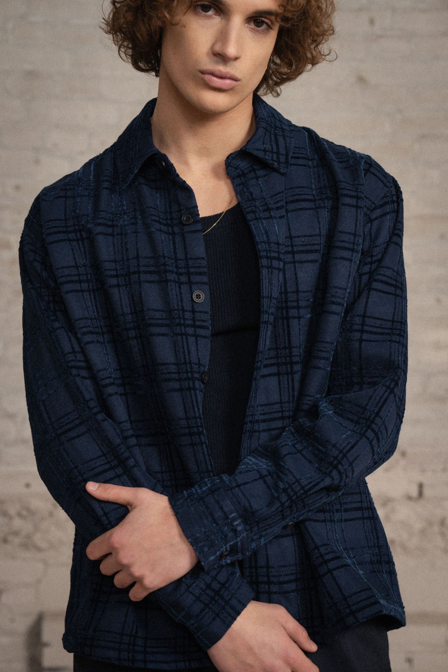 Young person wearing navy plaid jacket poses against textured wall in professional photo series.