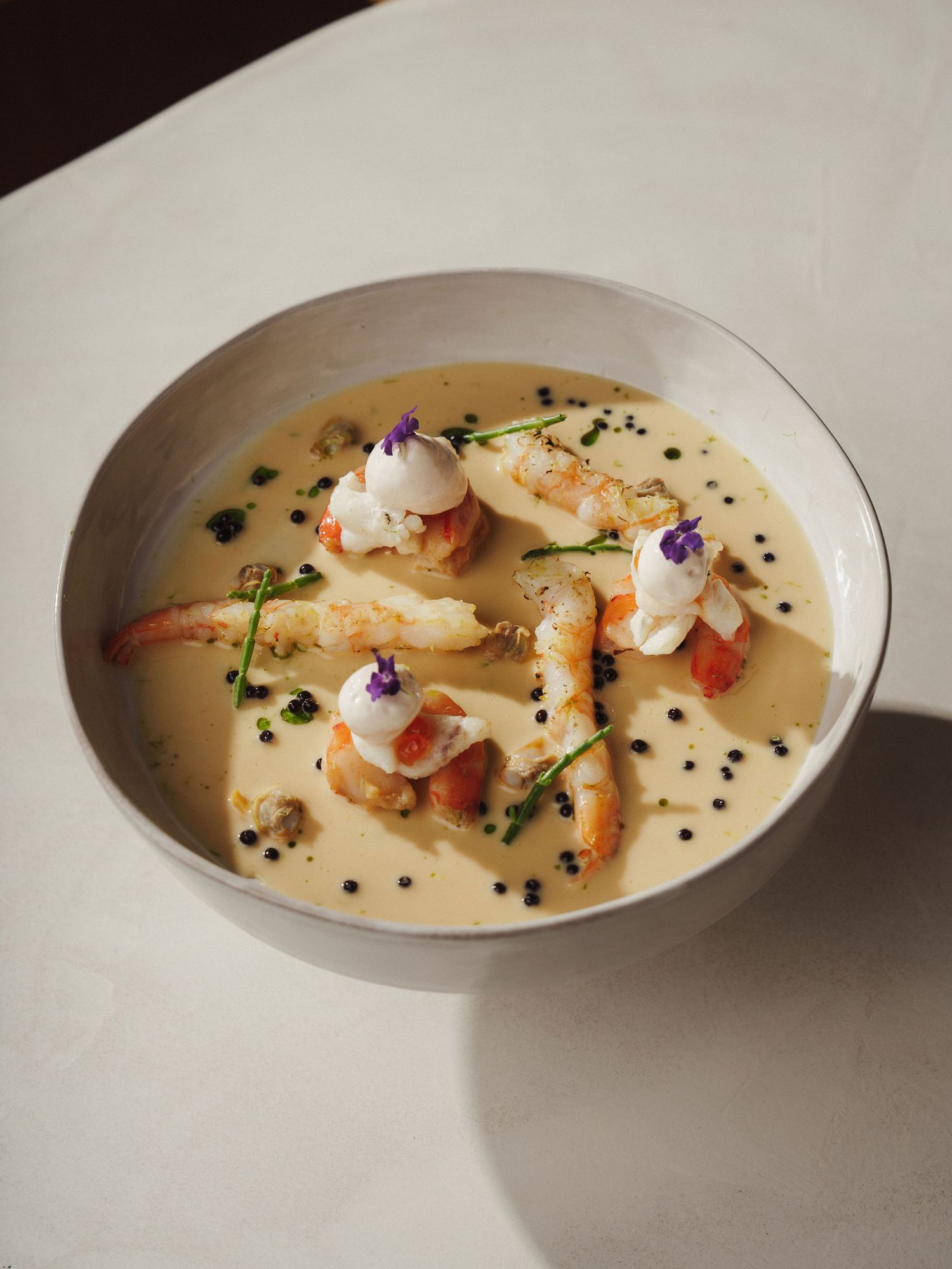 Elegant shrimp bisque with cream sauce, black caviar, whipped cream, and edible flowers in a white bowl.