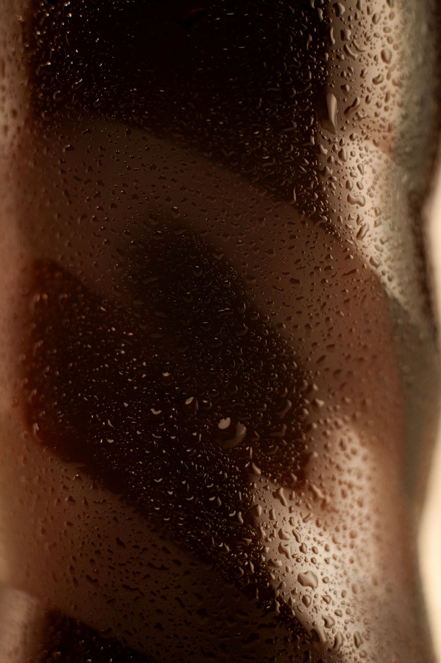 Close-up of a wet dark glass bottle with condensation droplets, warm brown tones, moody lighting.
