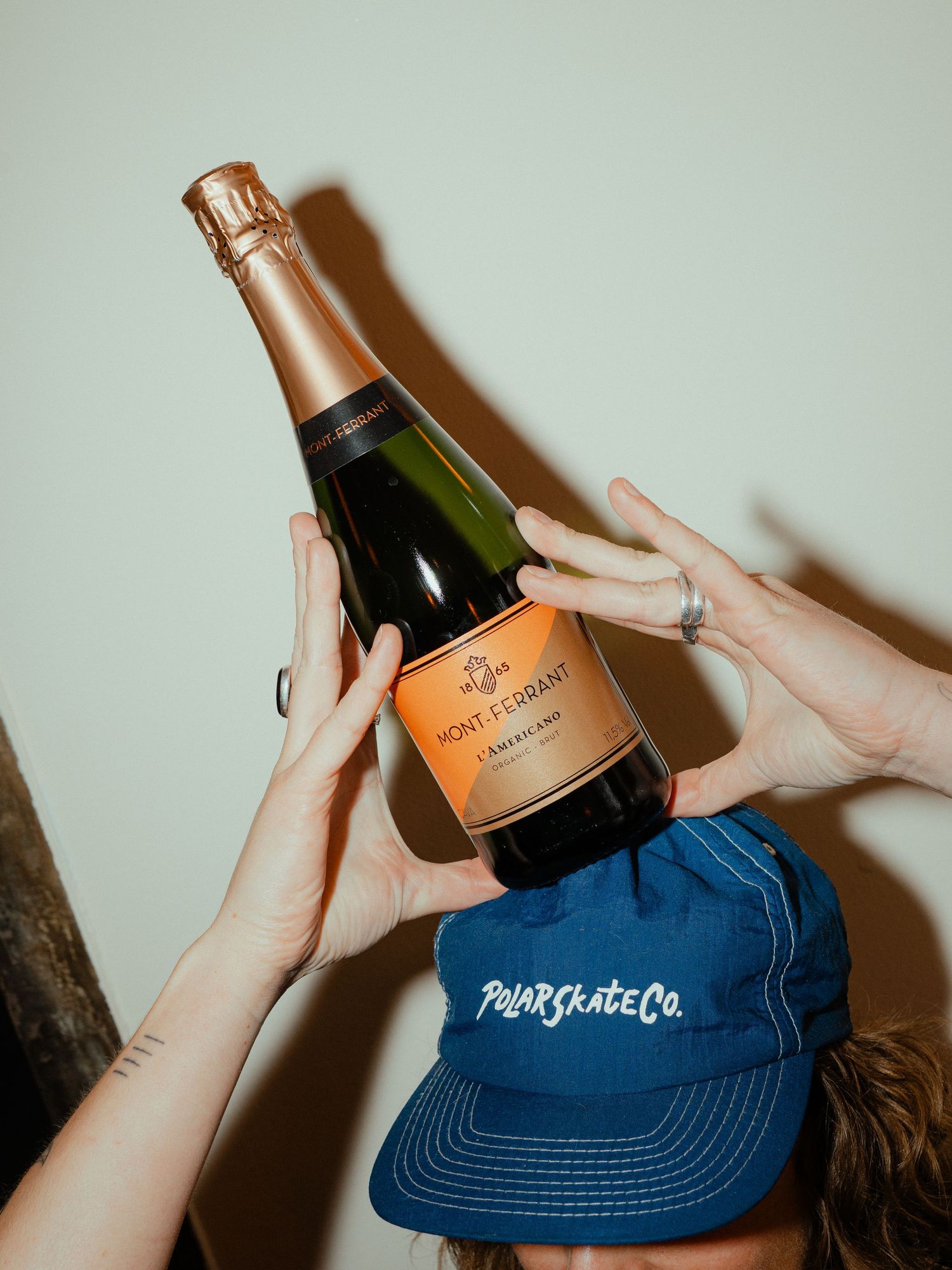 Hands balancing a Pont Ferrant Cremant sparkling wine bottle on a Polar Skate Co blue cap.