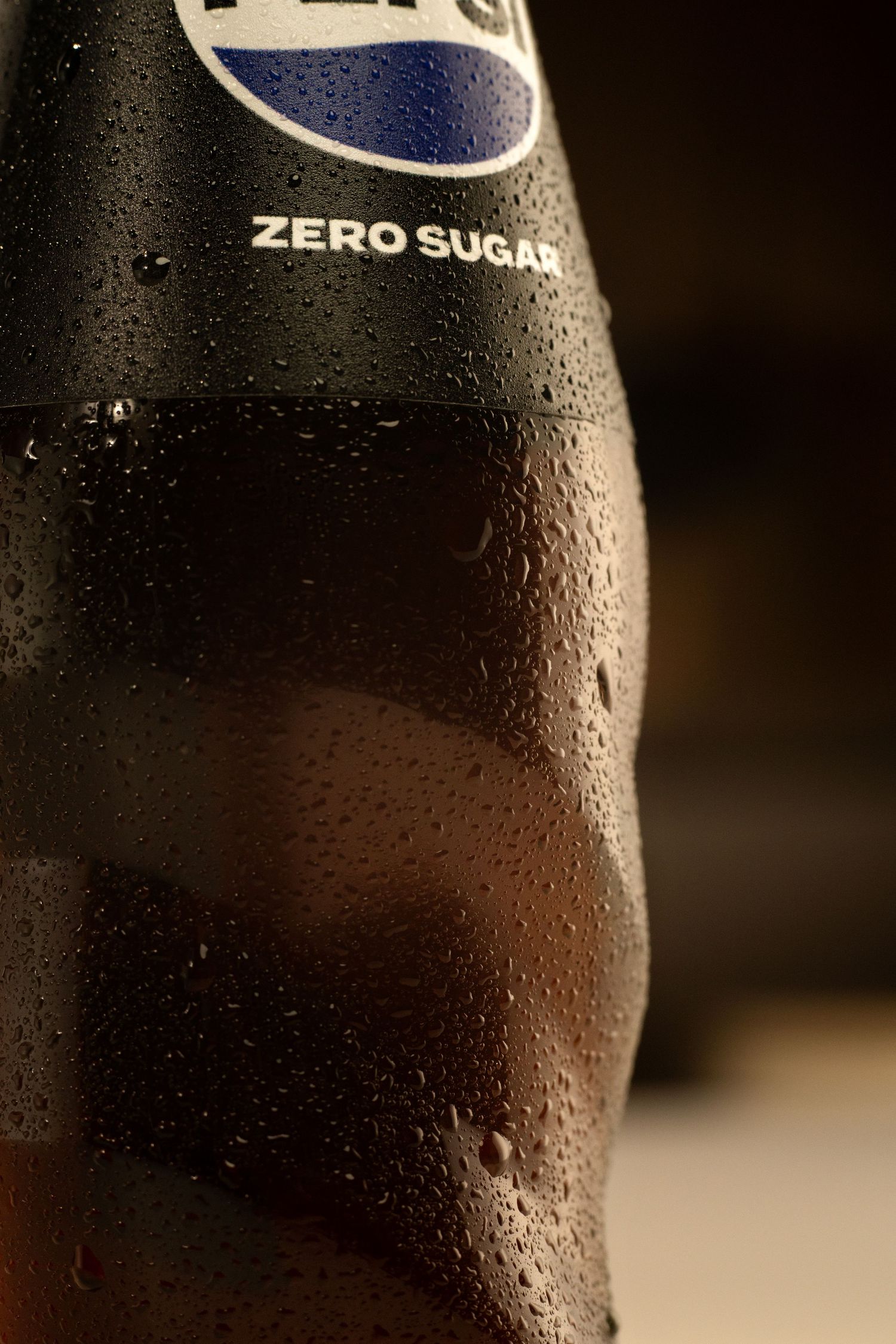 Close-up of a cold Pepsi Zero Sugar black bottle covered in water droplets on a dark background.
