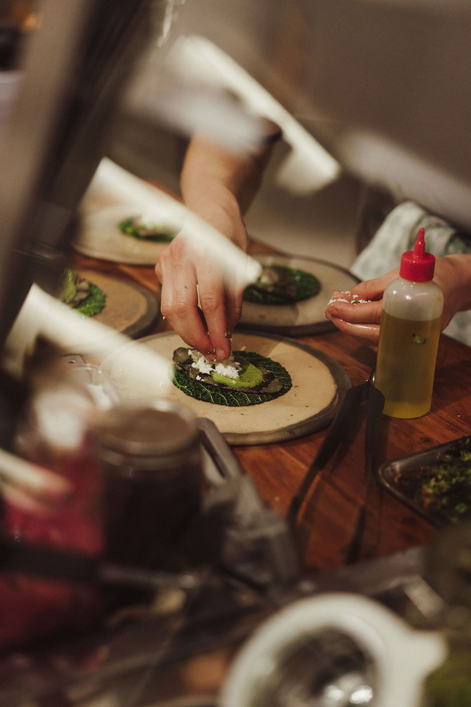 Chef carefully garnishing green leaf appetizers on wooden boards in a professional restaurant kitchen.