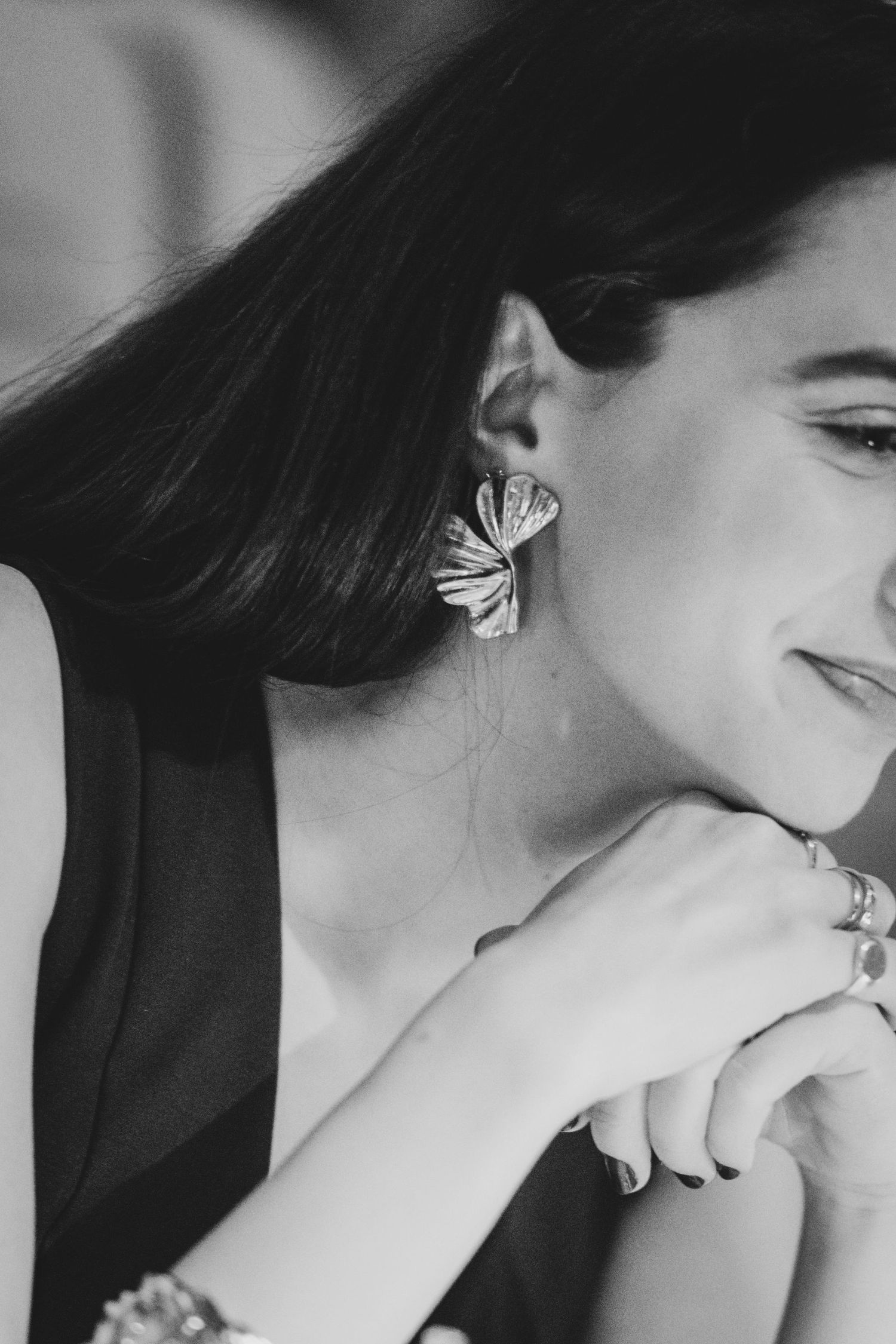Black and white portrait of a smiling woman wearing butterfly earrings and bracelets, hands clasped near her chin.