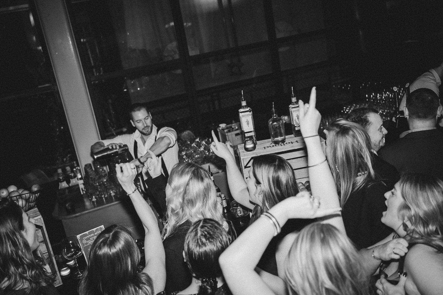 Black and white photo of a bartender serving drinks to a lively crowd at a nightclub party.