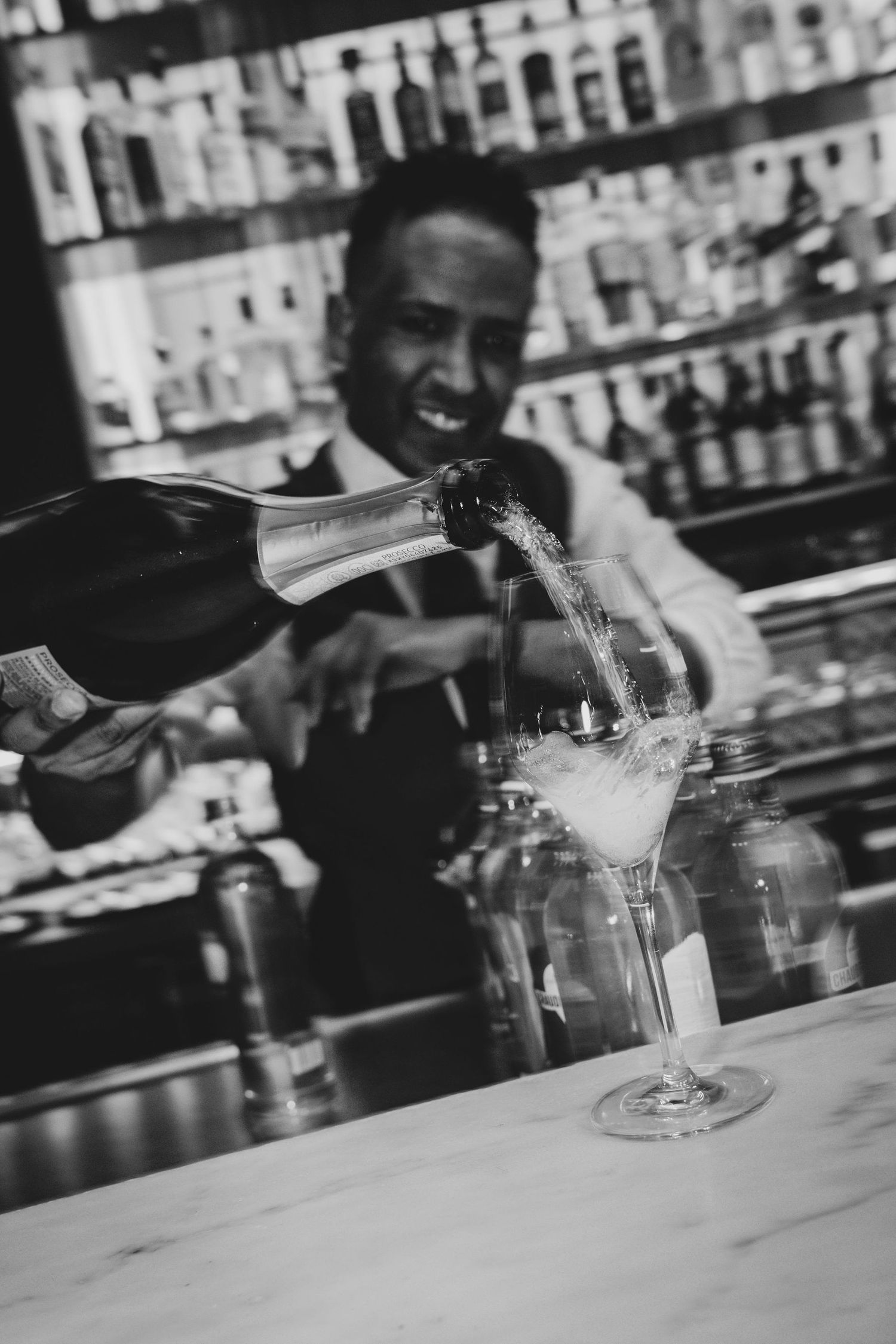 Bartender pouring champagne into elegant martini glasses at a upscale bar in black and white photo.
