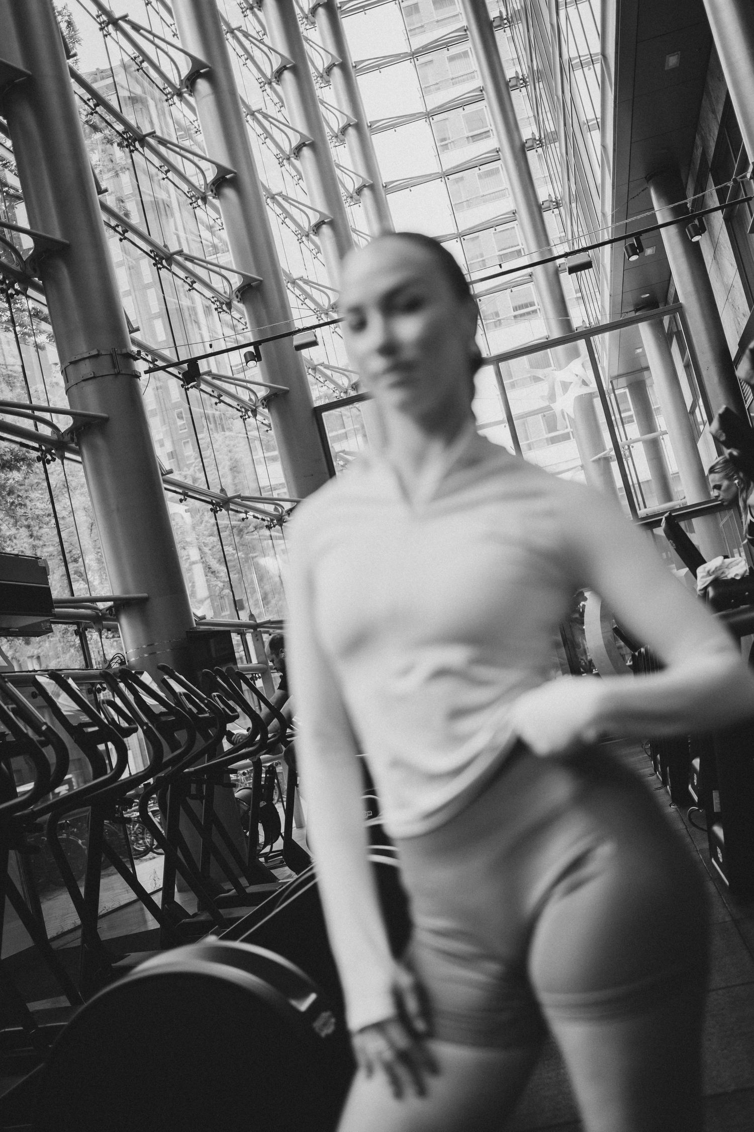 Black and white photo of a fit woman in athletic wear working out in a modern gym with large glass windows.