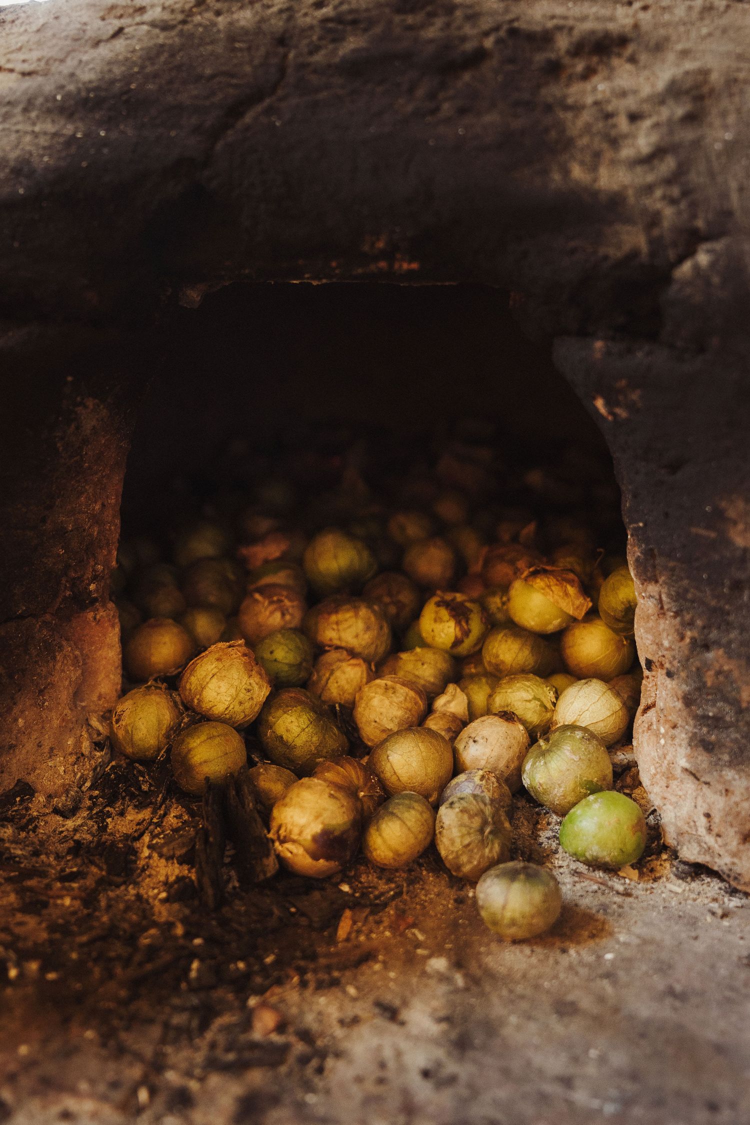 Tomatillos roasting inside a rustic stone oven, bathed in warm light for traditional Mexican cooking.