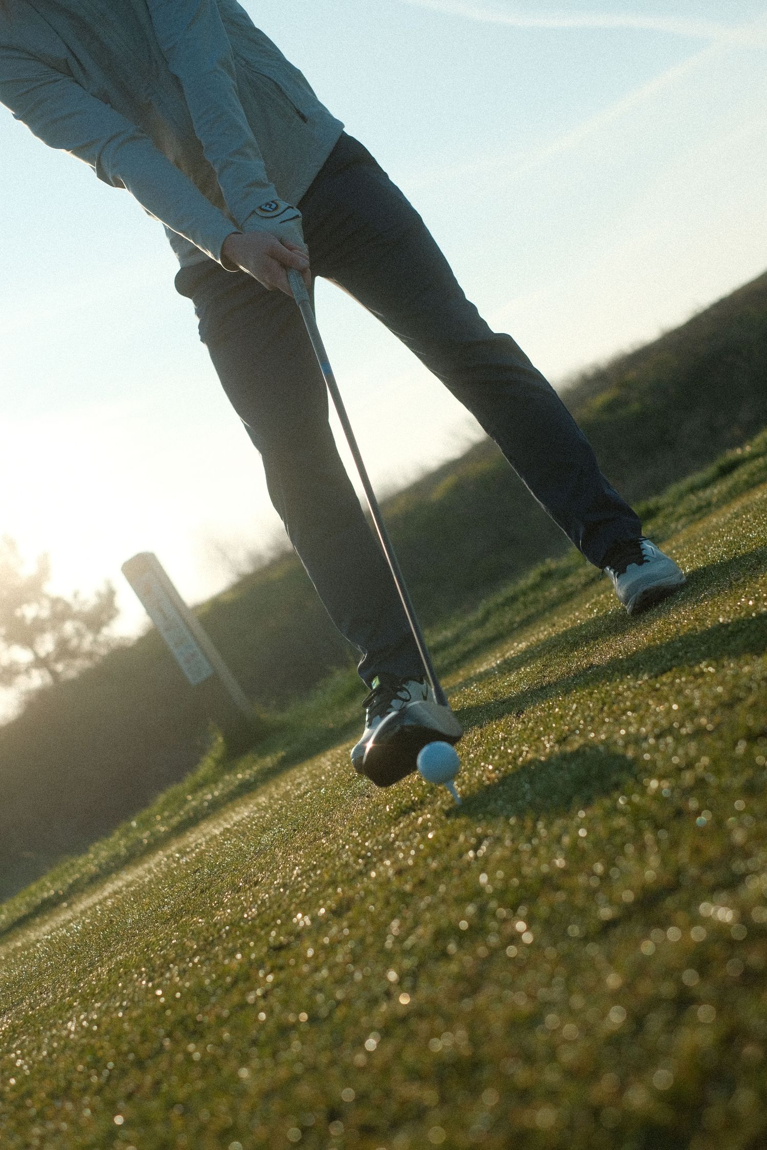 Golfer preparing to swing a golf club on a sunlit green course with a golf ball on the ground.
