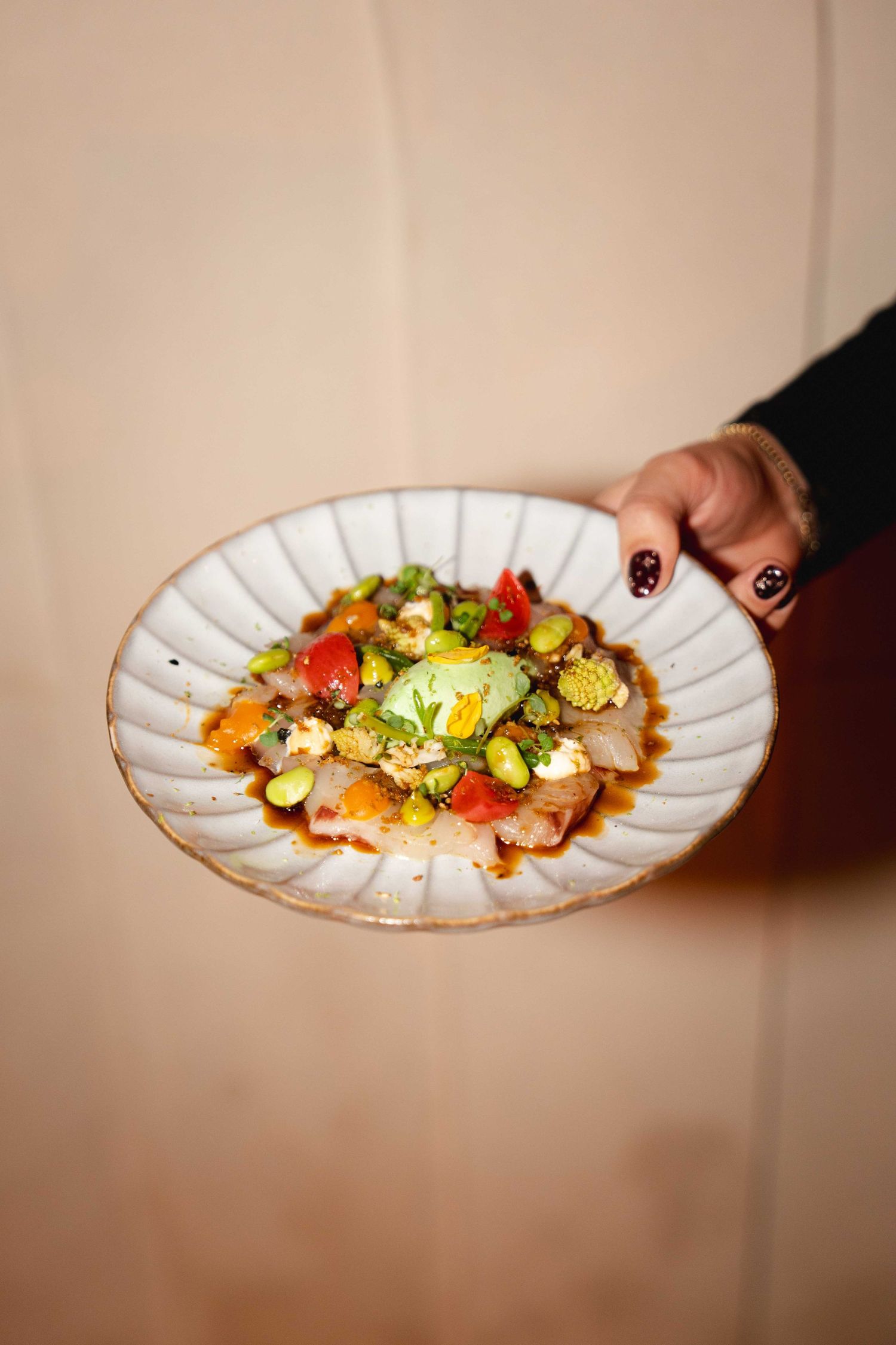 Hand holding a white ceramic plate with a colorful gourmet salad dish.