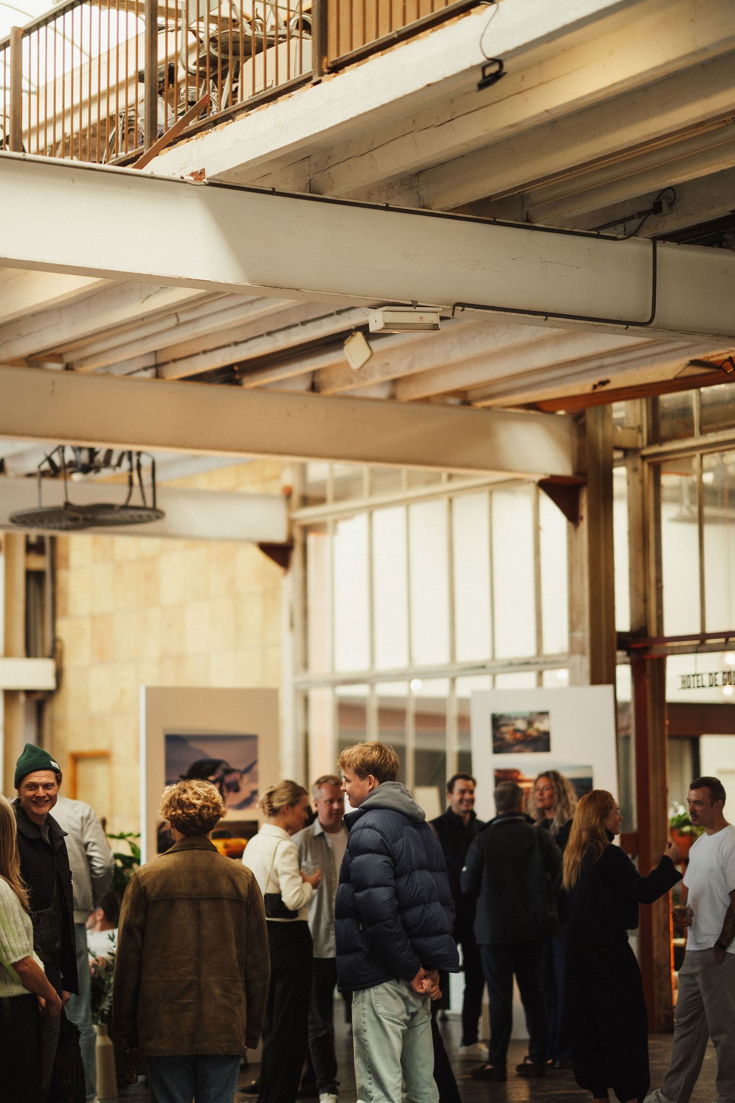 People mingling at an indoor art exhibition in a modern industrial venue with warm natural light.