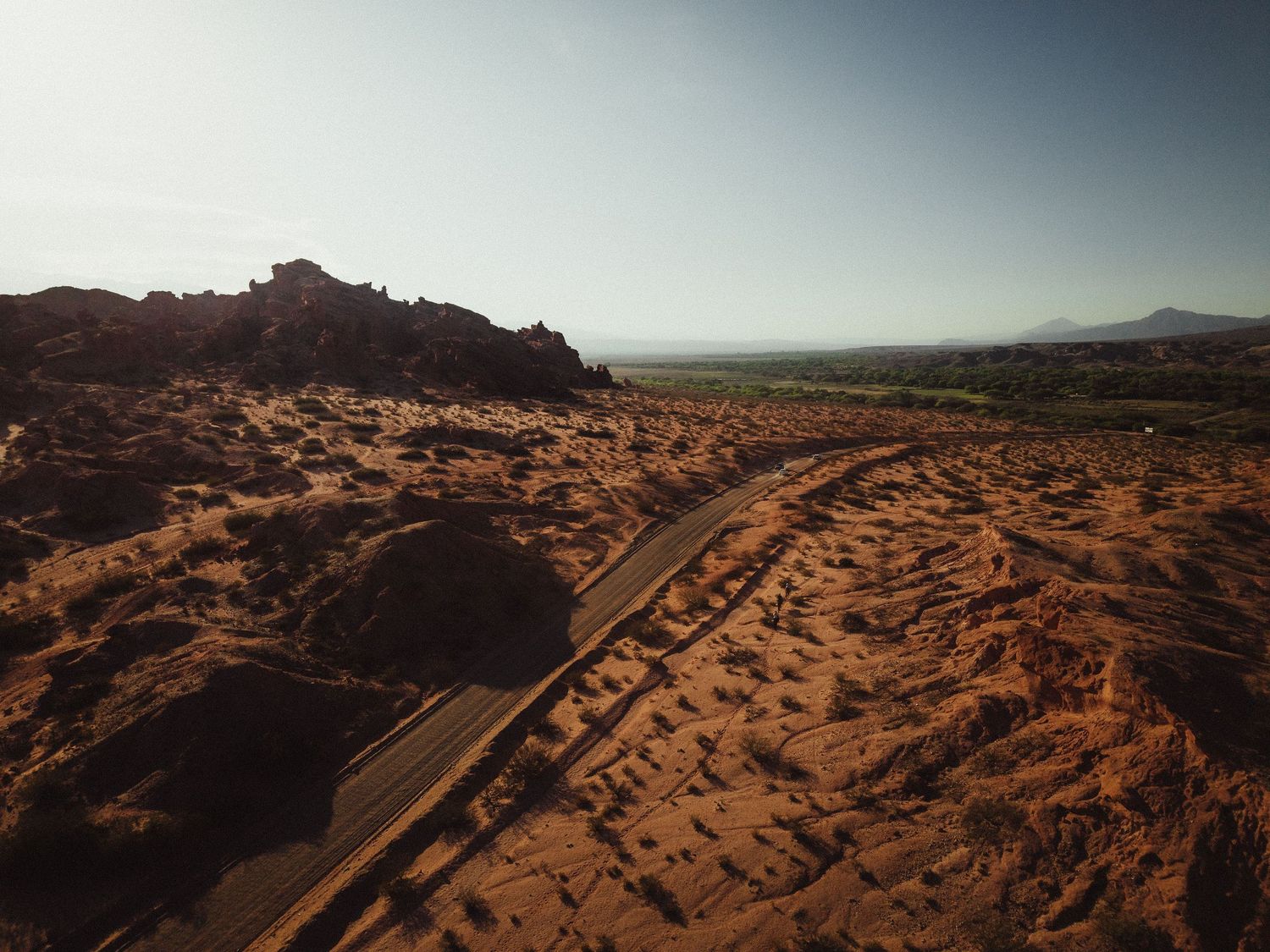Aerial view of a winding road through vast red desert landscape with rocky formations under a clear sky.