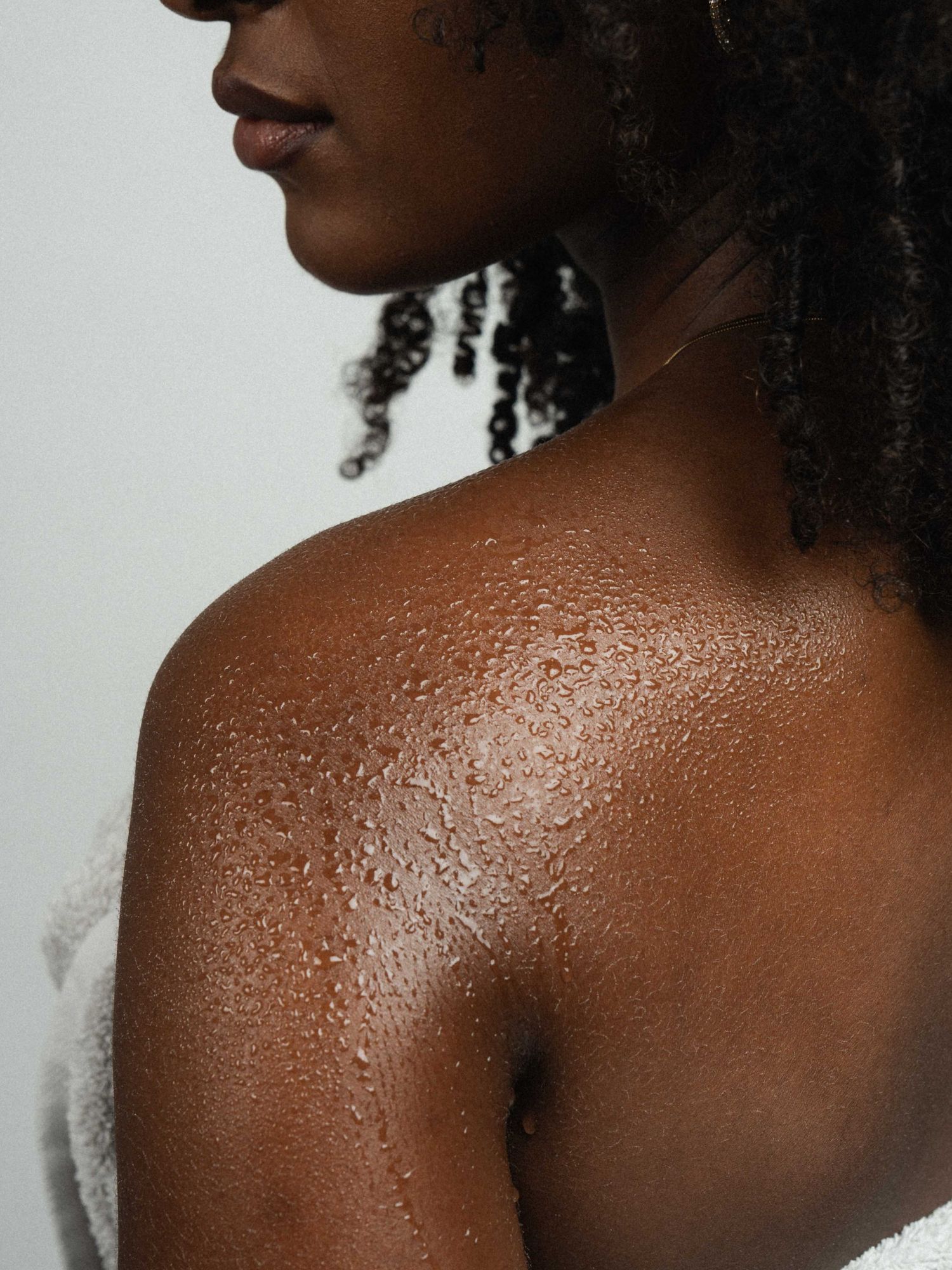 Close-up of water droplets on a Black woman's bare shoulder and back against a light background.