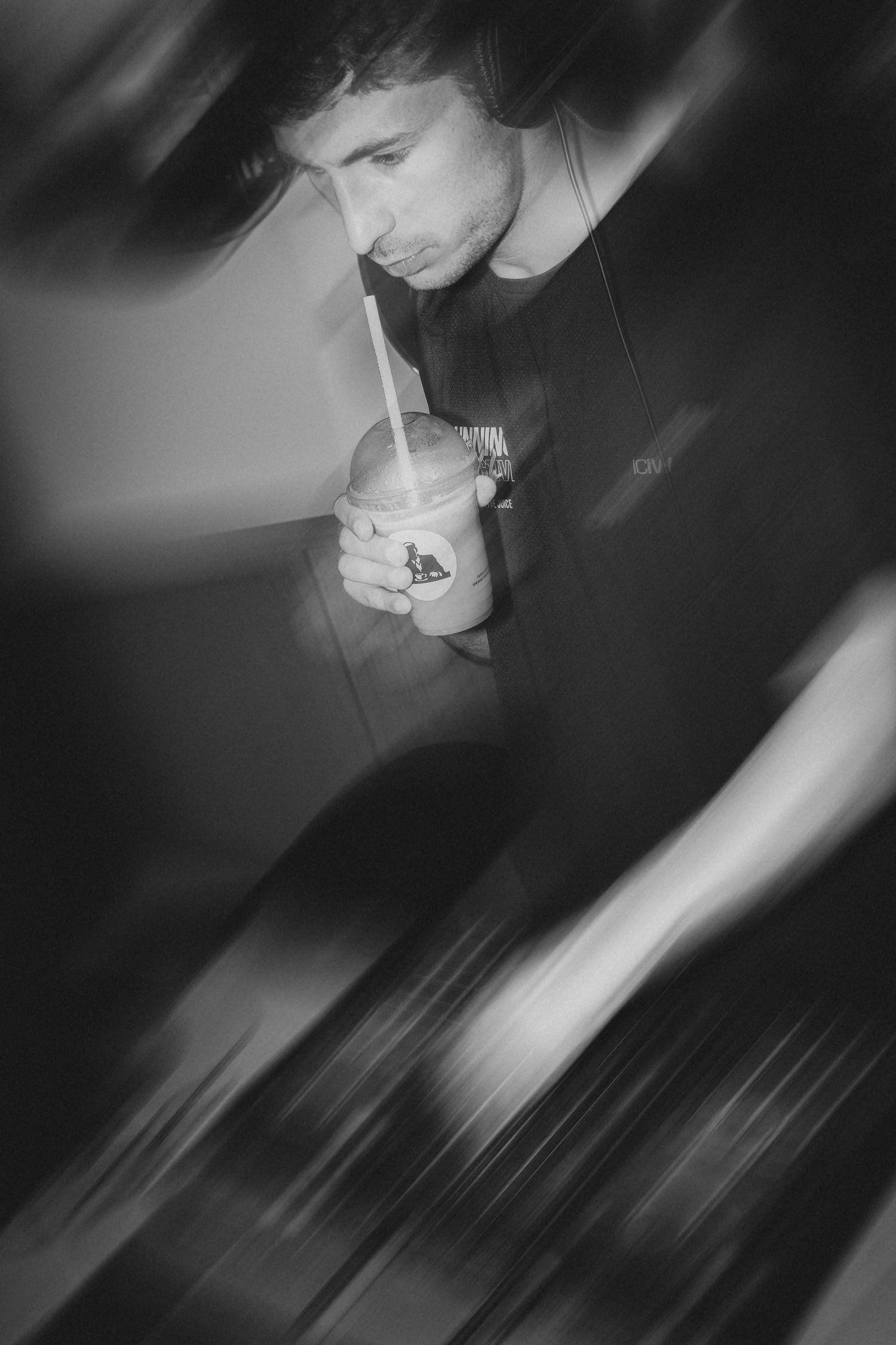 Black and white photo of a young man drinking from a cup with a straw, motion blur effect.