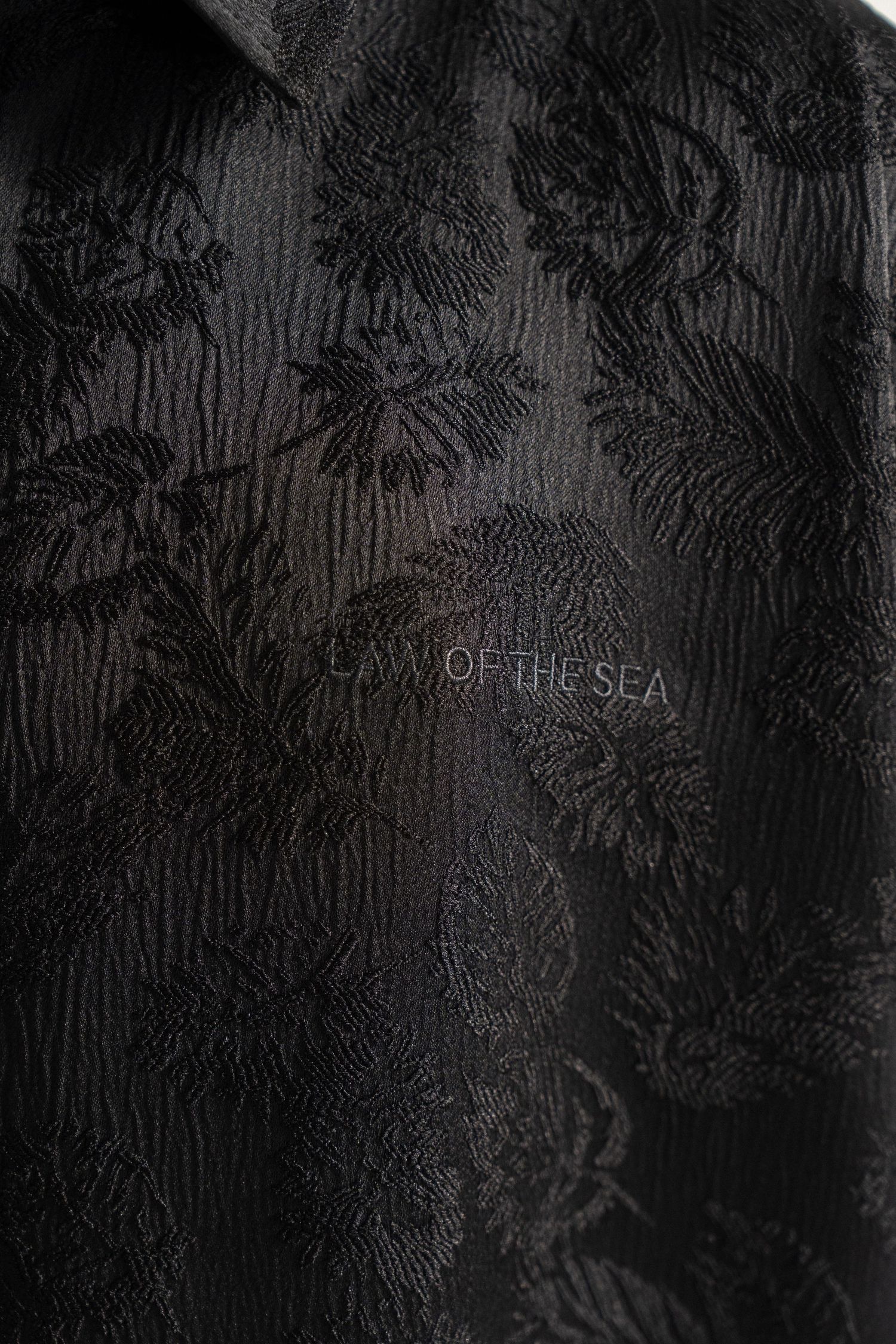 Close-up of dark textured fabric with embossed floral pattern and text 'OF THE SEA' visible.